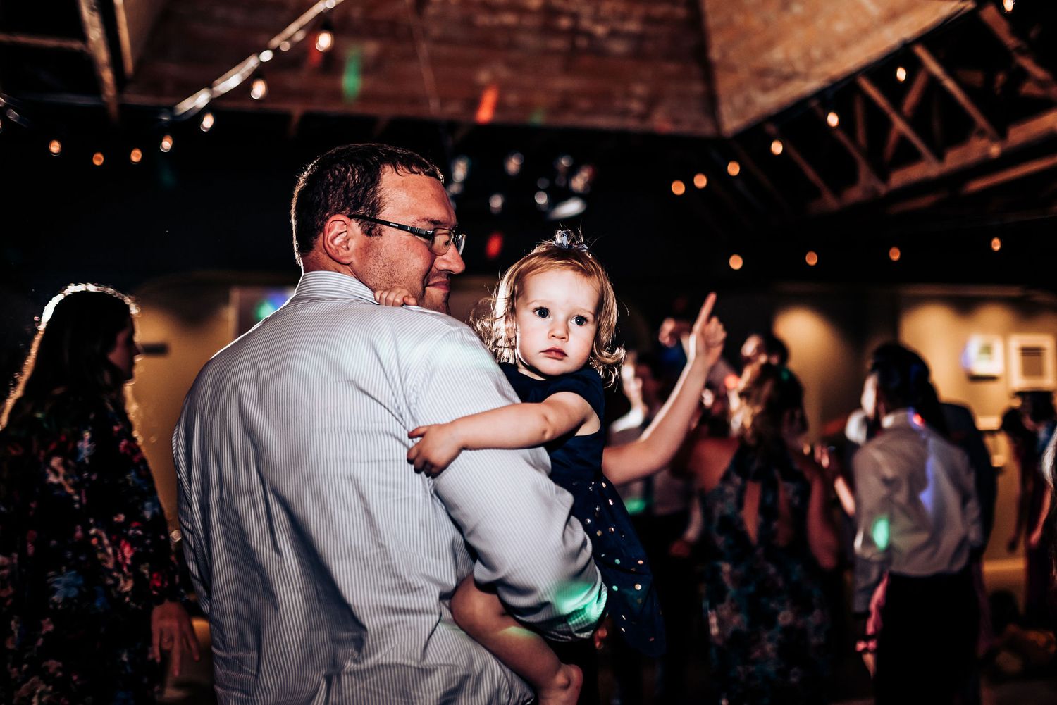 Adult holding a small child while dancing at a wedding reception.