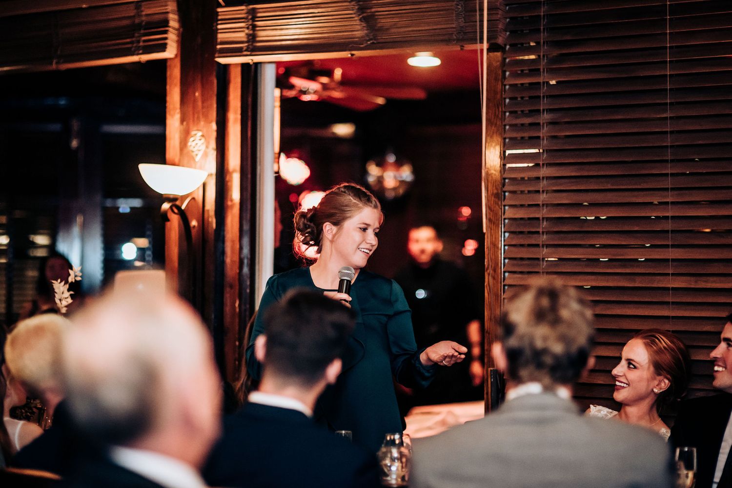 A person stands to make a speech during a wedding reception dinner.