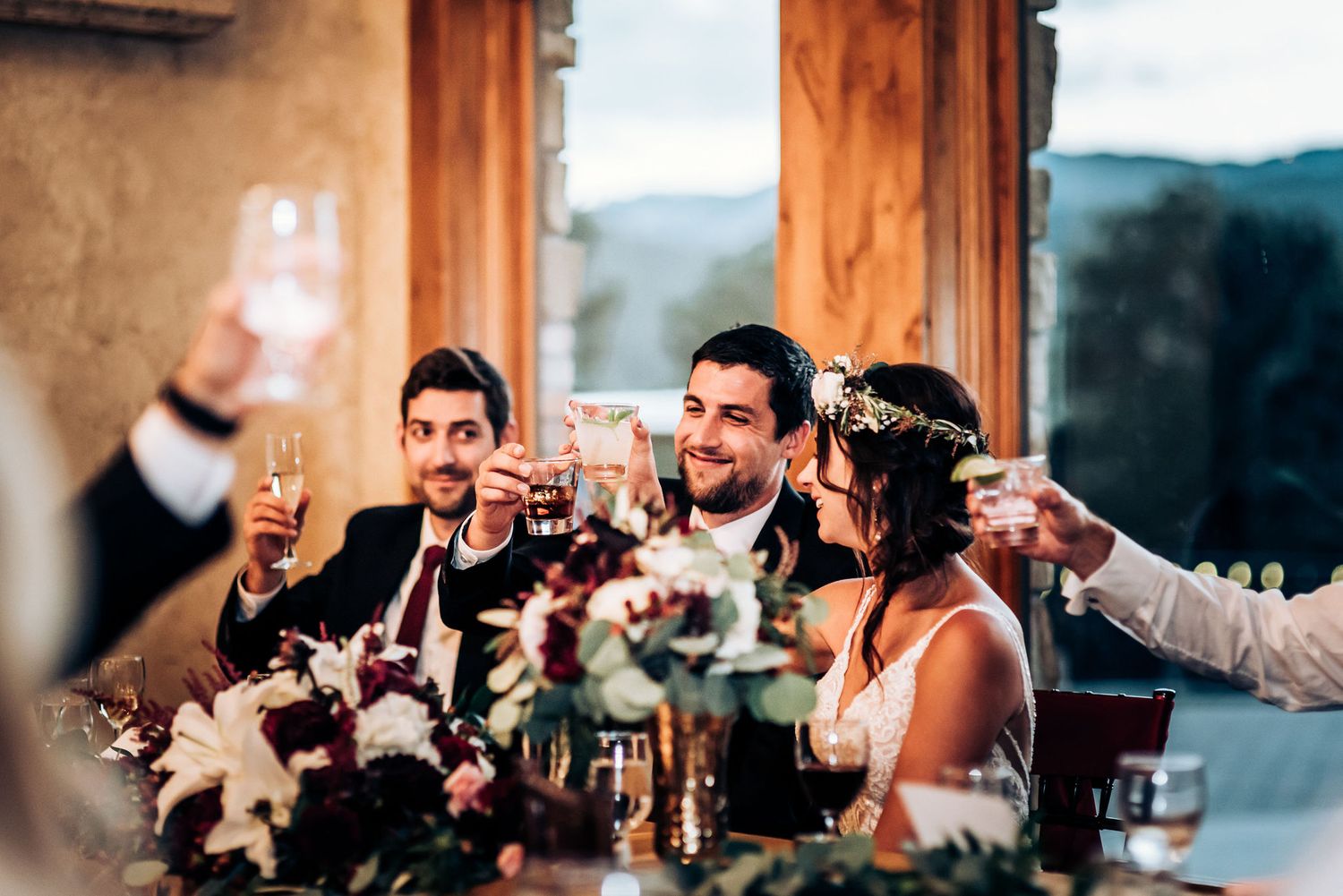 Wedding party toasting during reception with mountain view through windows.