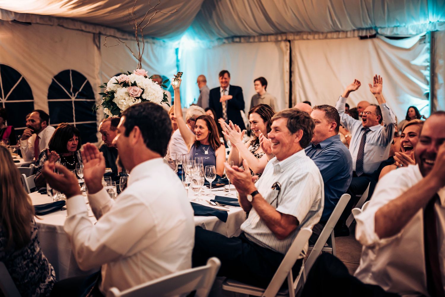 Wedding guests applauding during reception celebration in tent.