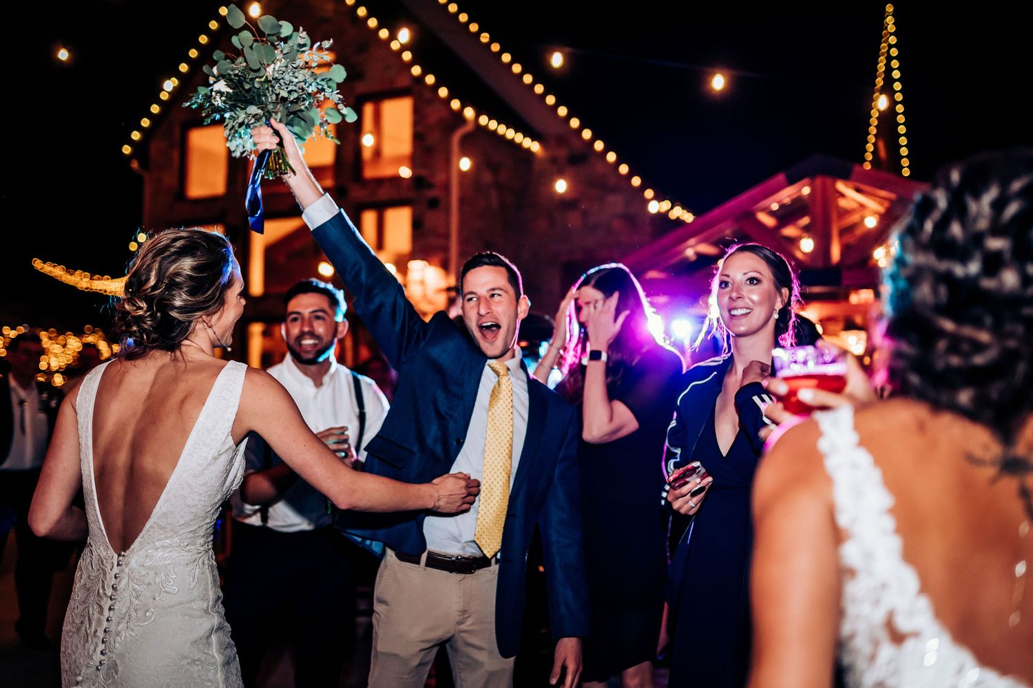 Celebratory moment at outdoor wedding reception with guests cheering under string lights.