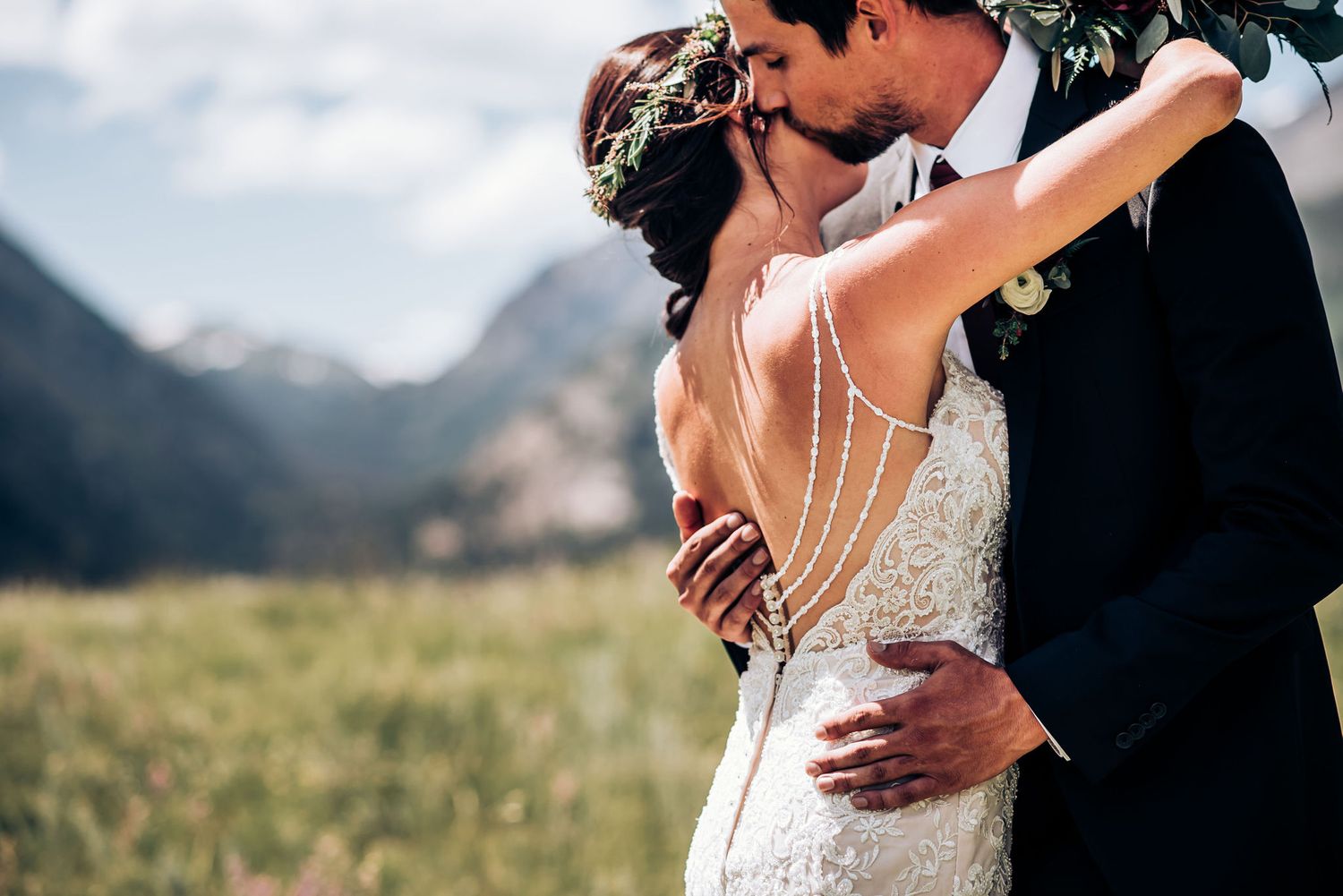 An intimate wedding kiss between newlyweds against a mountain backdrop in a scenic meadow.