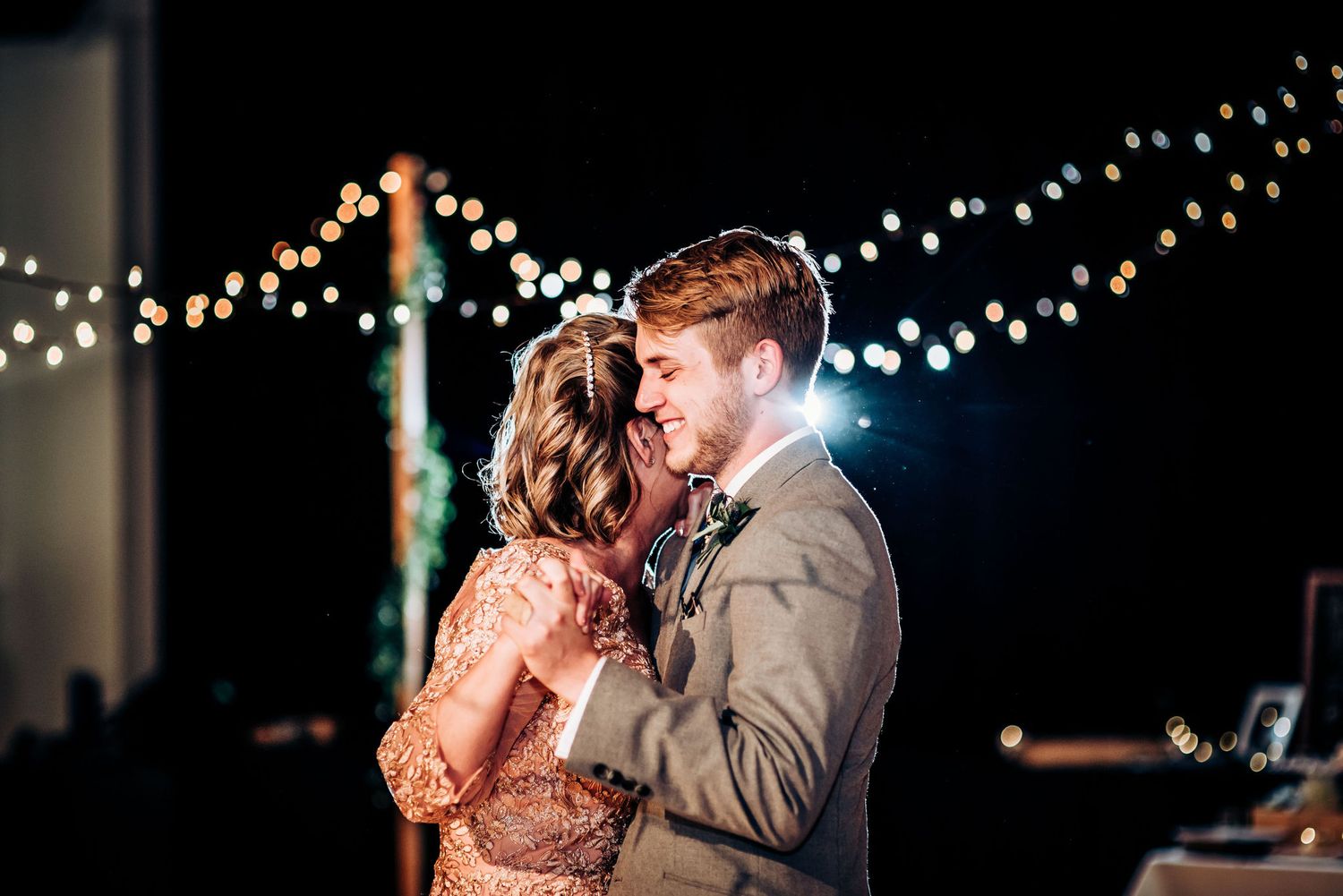 Dancing couple in formal attire illuminated by romantic fairy lights at evening reception.