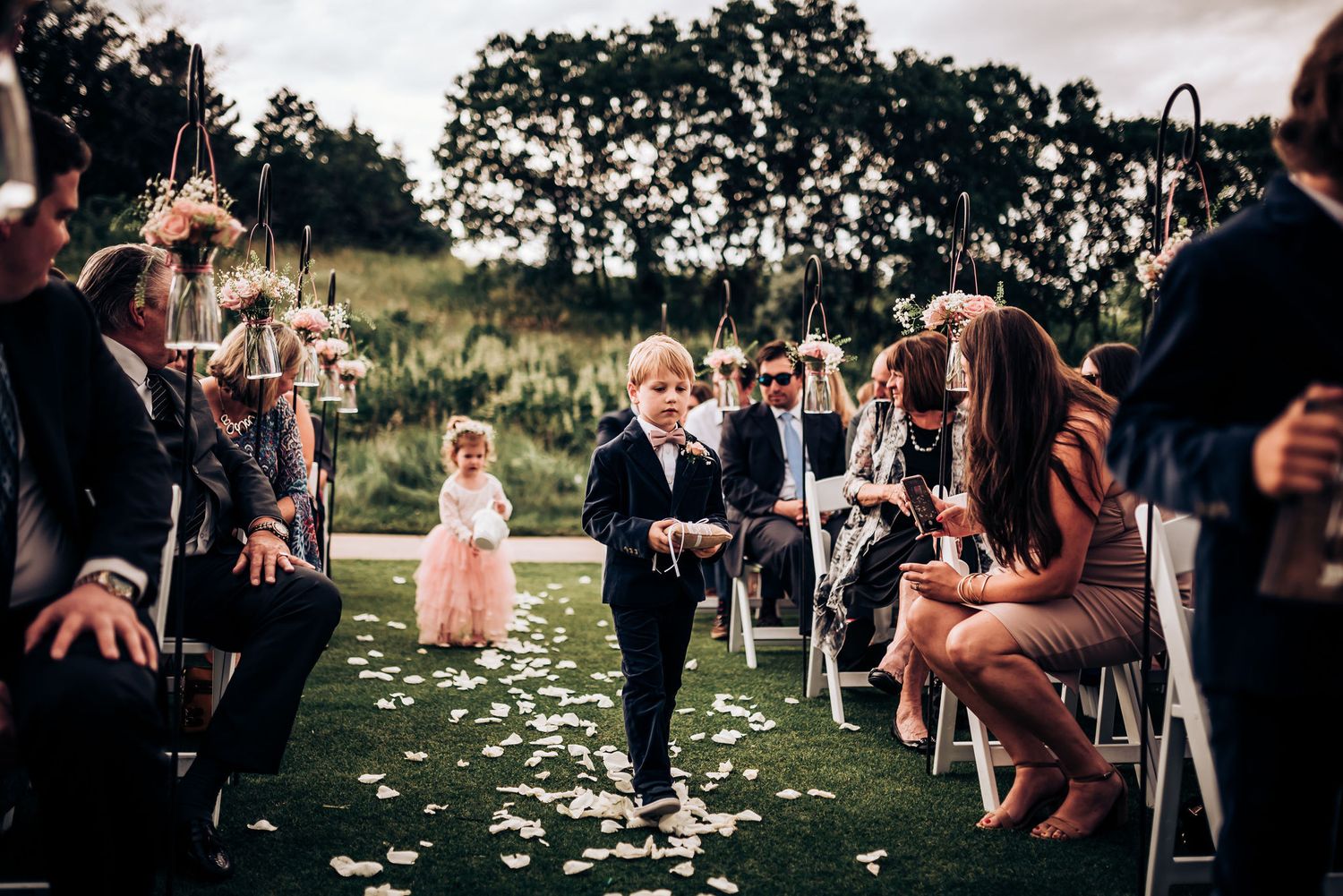 Outdoor wedding ceremony with guests seated along flower-petal covered aisle.