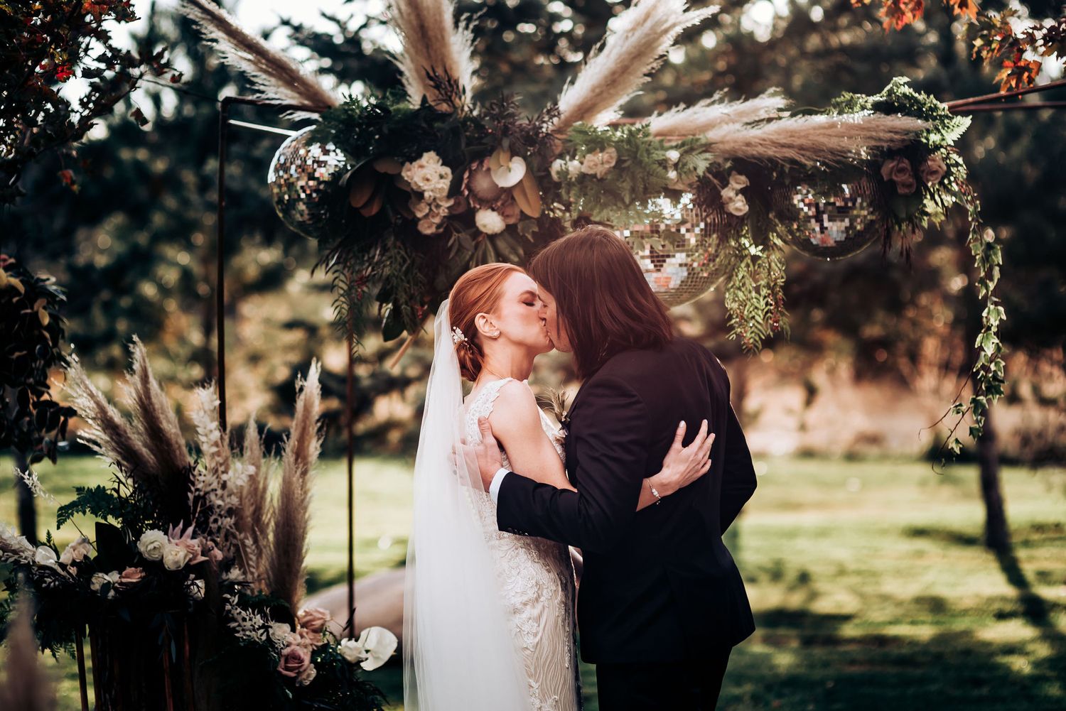 Romantic embrace during outdoor wedding ceremony under floral arch with sunlight.
