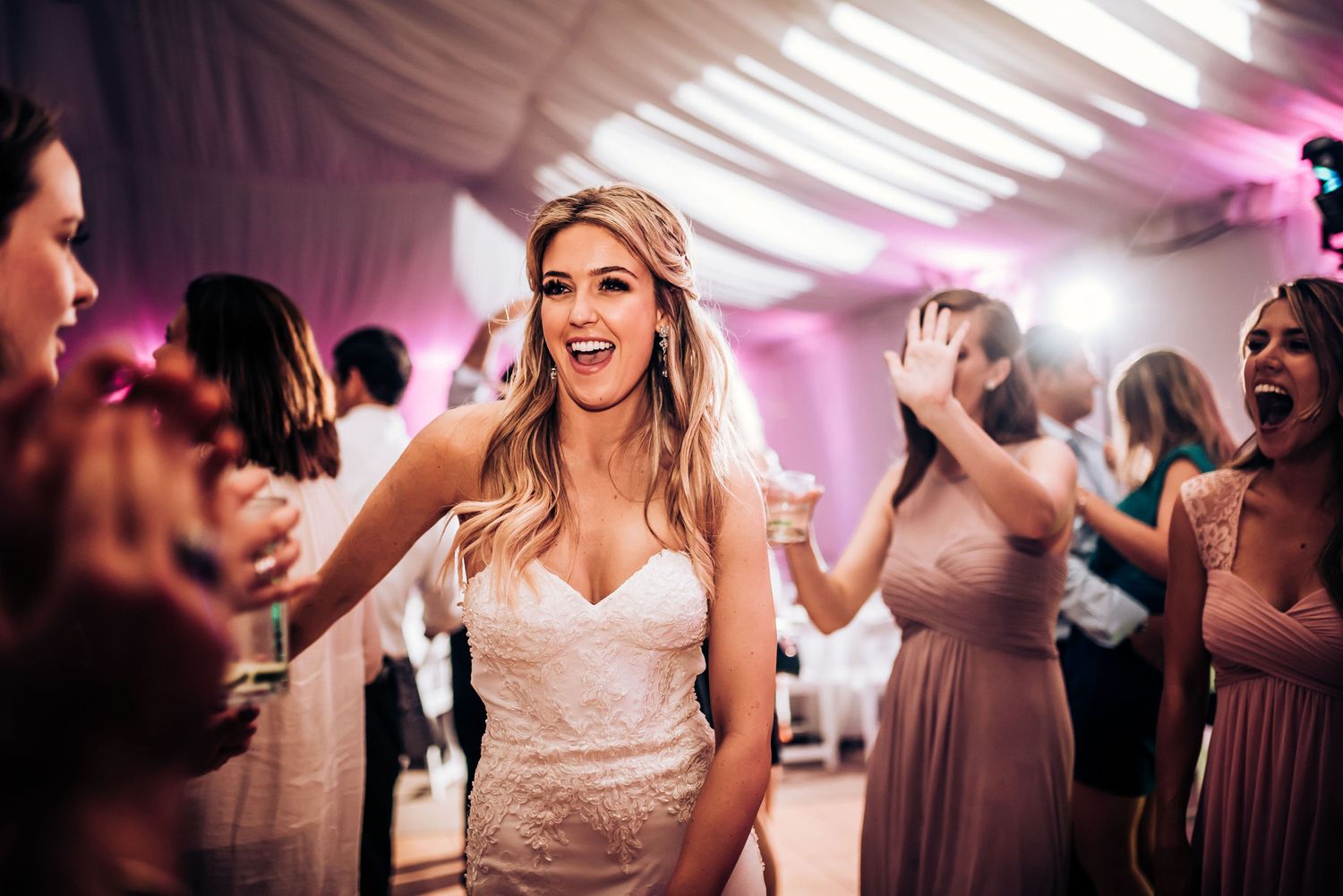 Bride dances joyfully among guests at wedding reception under white tent.