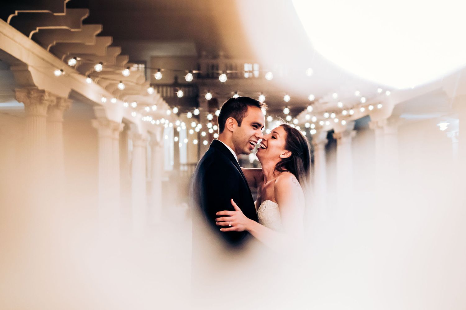 An intimate wedding portrait with a dreamy vignette effect and twinkling lights overhead.