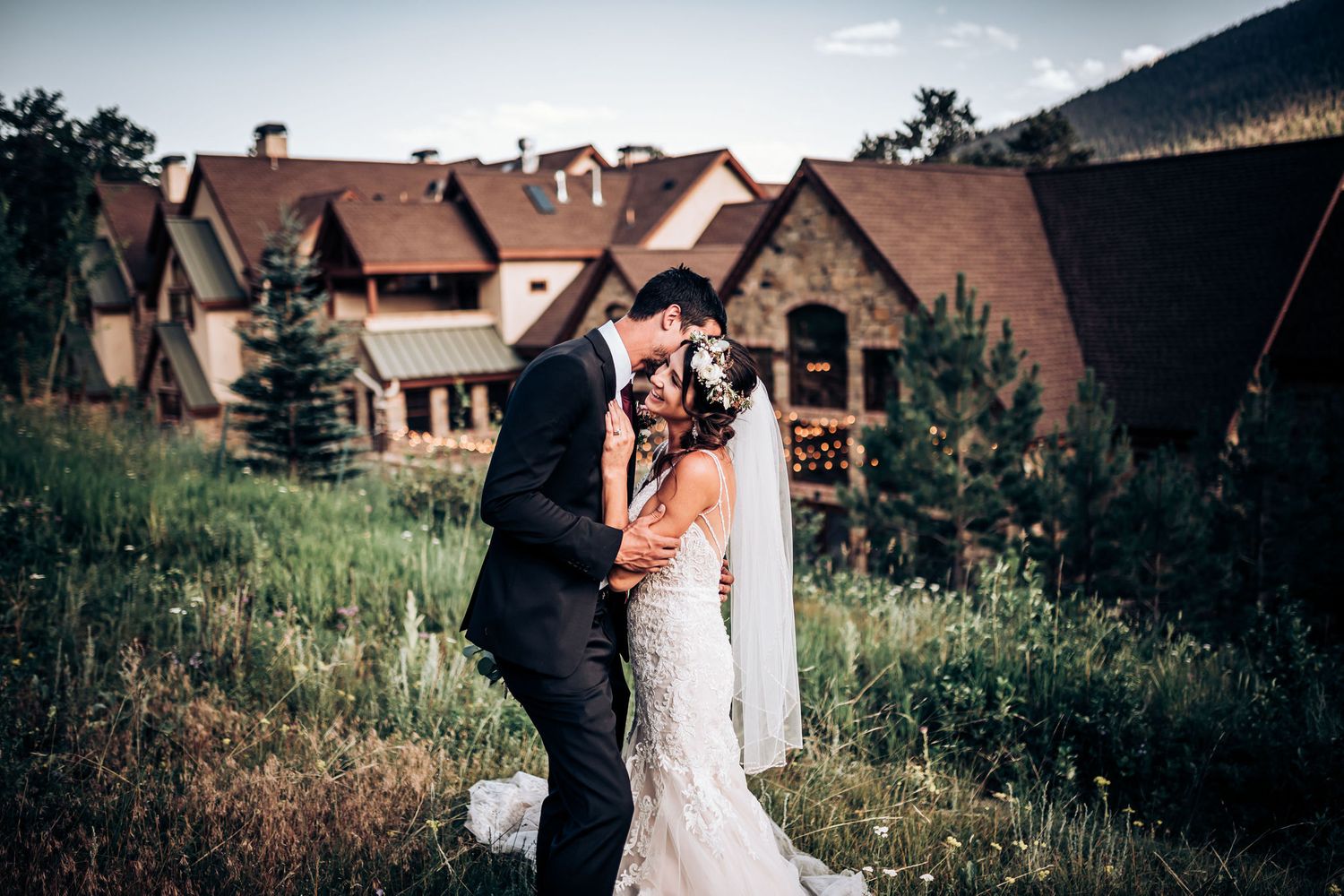 Romantic wedding scene with mountain lodge buildings in background.