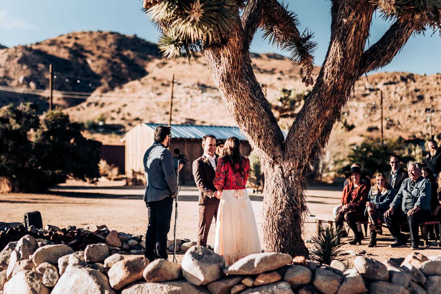 Wedding ceremony taking place in a desert setting with rock borders and Joshua trees.