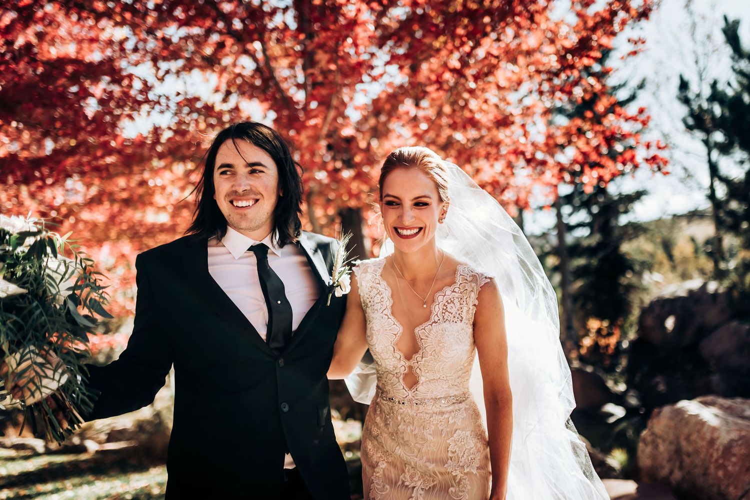 Happy wedding couple posing under red autumn trees in outdoor setting.