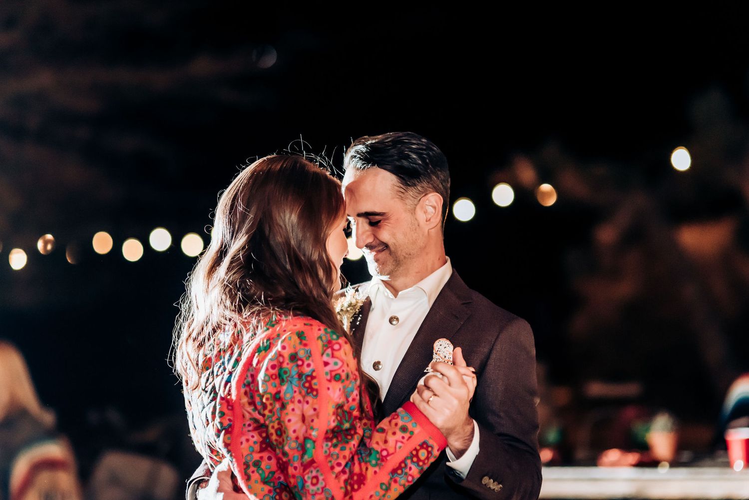Romantic couple shares an intimate dance moment under twinkling outdoor lights.