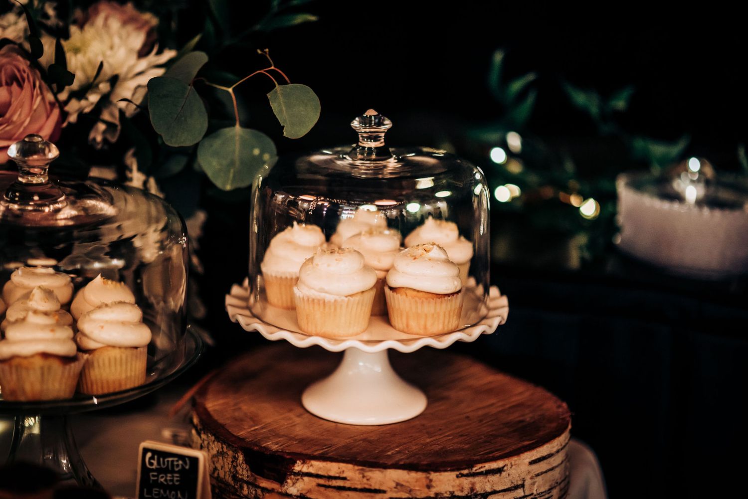 Cupcakes displayed under glass dome on wooden slice centerpiece with greenery accents.