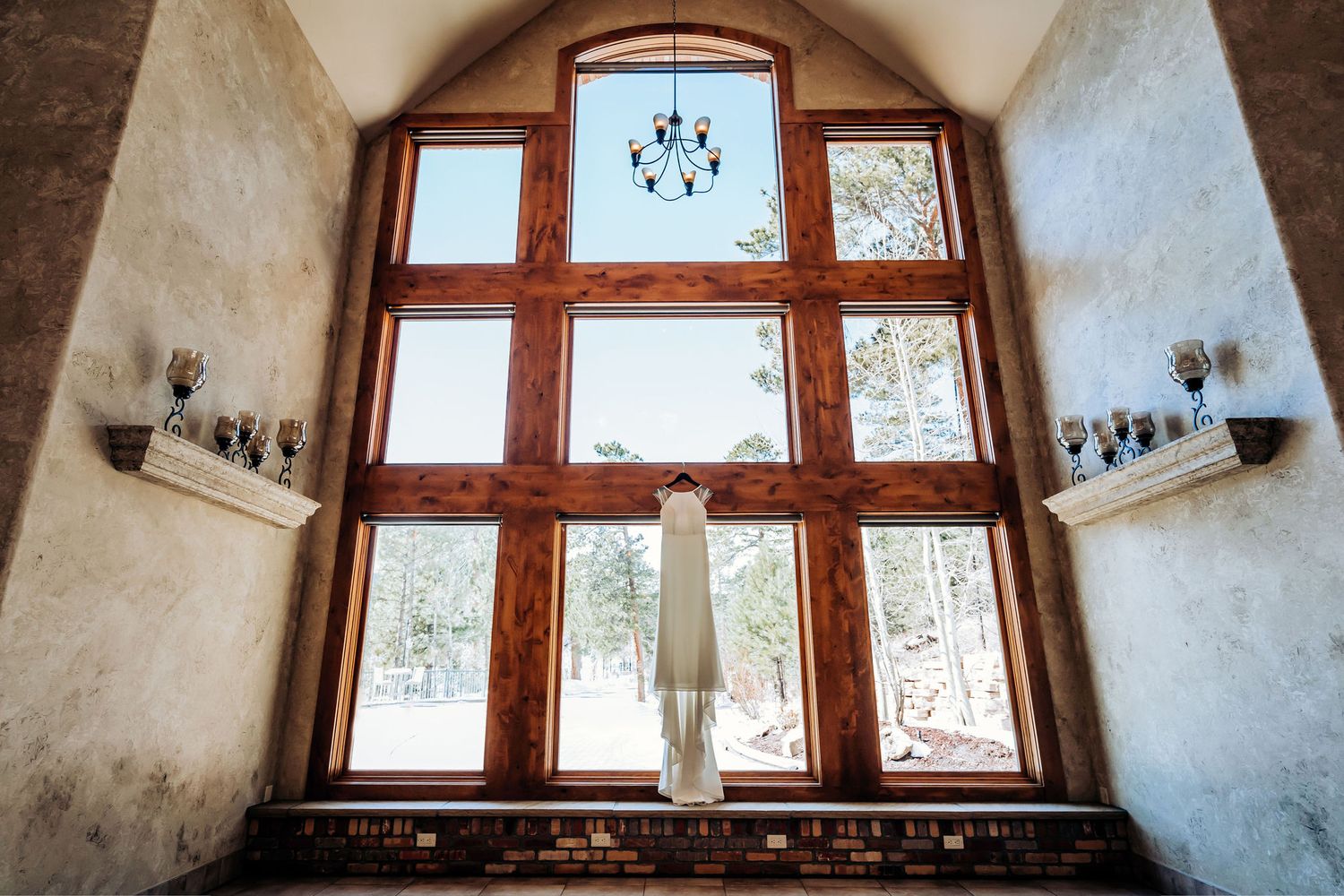 Elegant arched window with wooden frames and chandelier in a bright white wedding venue.
