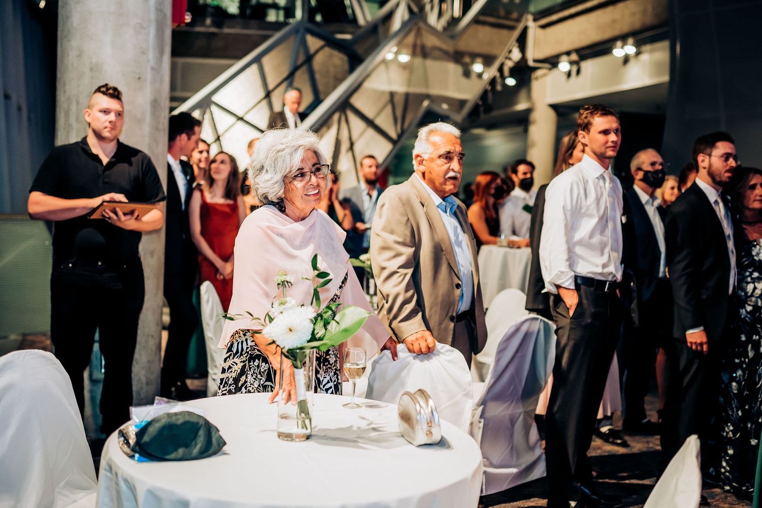 Wedding guests gather around elegant table settings at a modern venue.