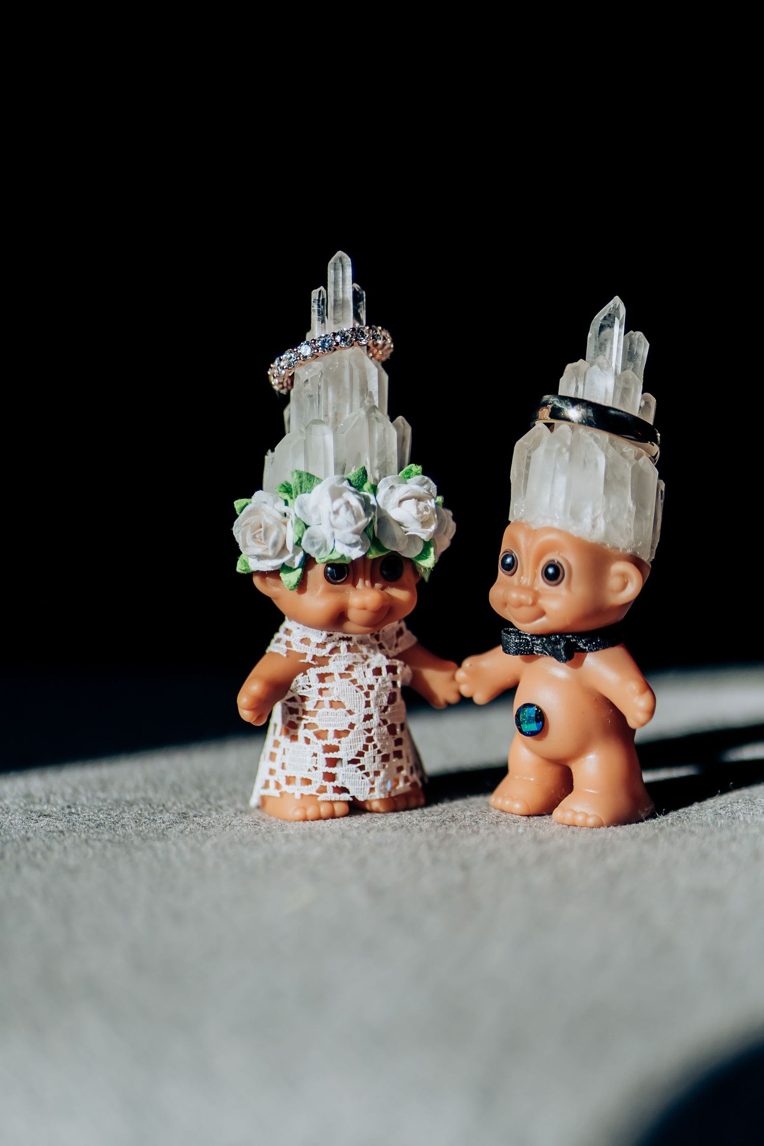 Two vintage troll dolls decorated with crystal crowns and white roses.