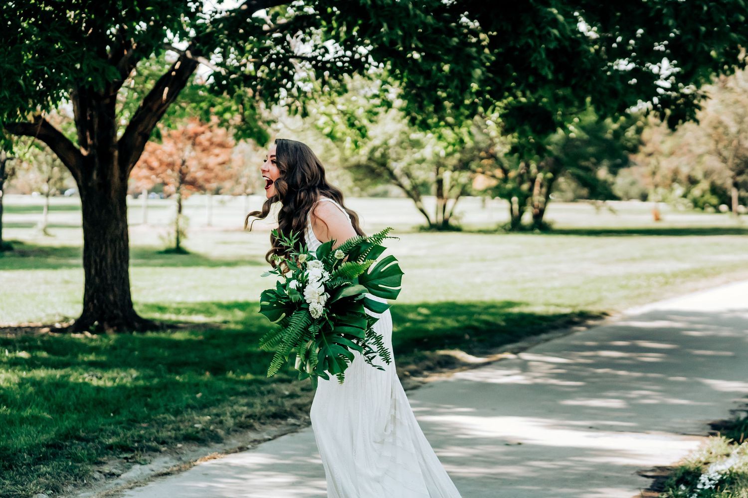 A flowing white wedding dress contrasts with vibrant green foliage in an outdoor garden setting.