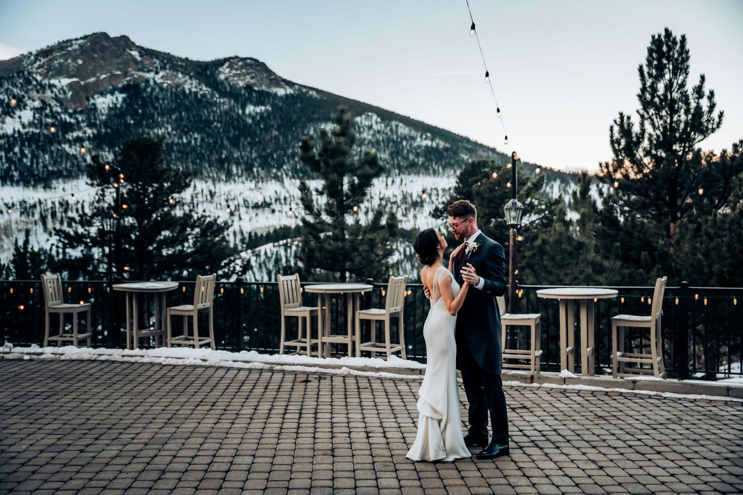 Couple shares a dance on an outdoor terrace with snow-capped mountains in the background.