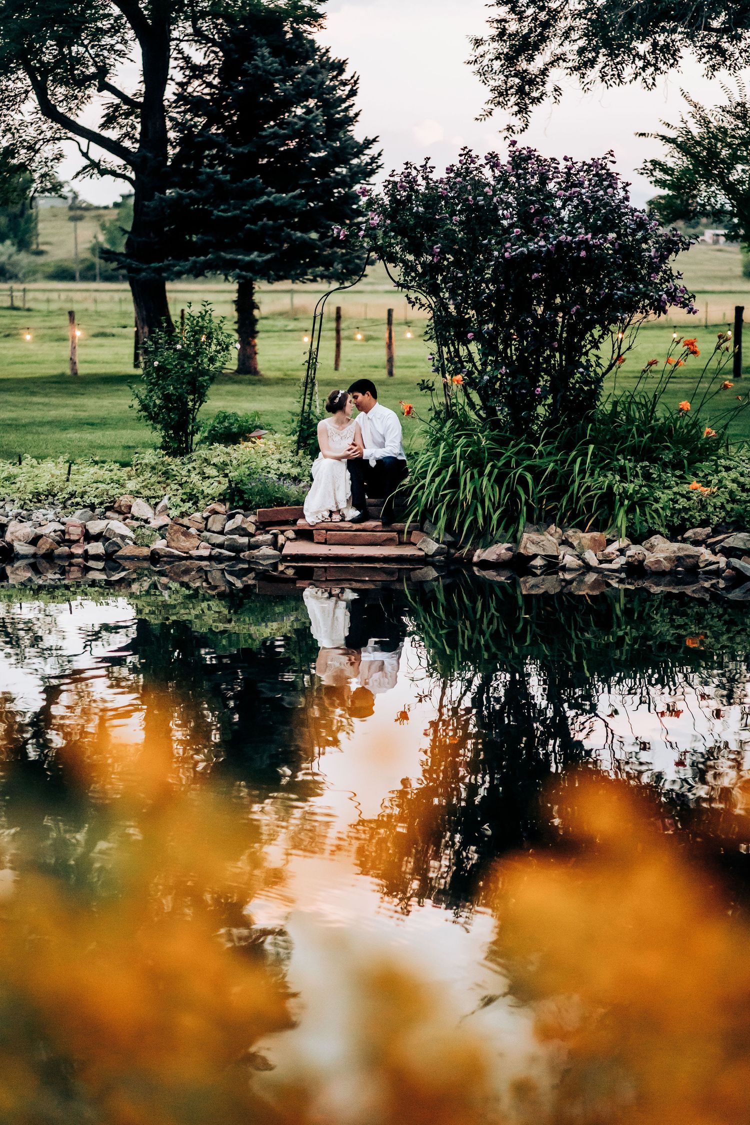 A romantic scene by a reflective pond with garden landscaping during golden hour.