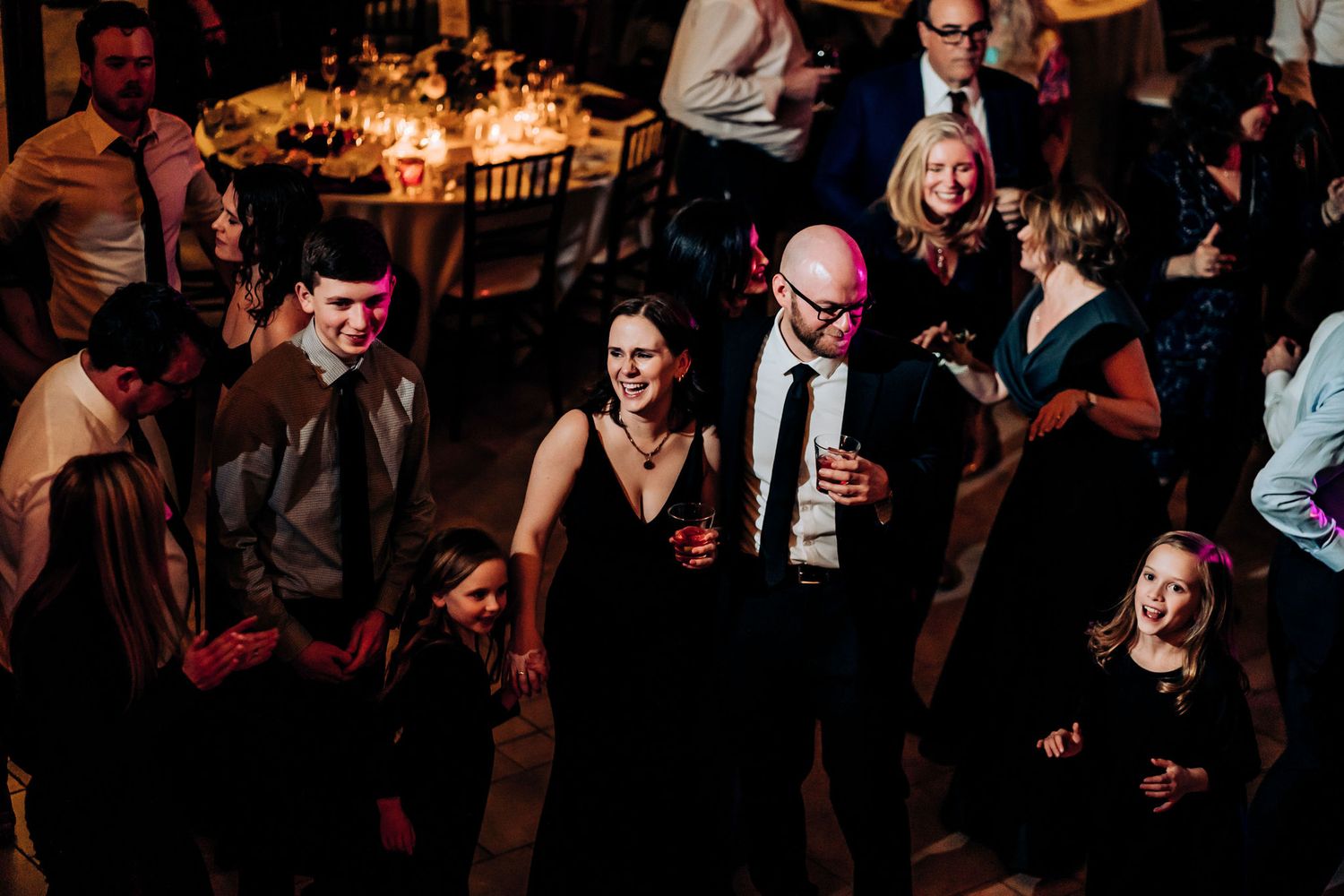 Party guests dance and socialize in a dimly lit reception venue.