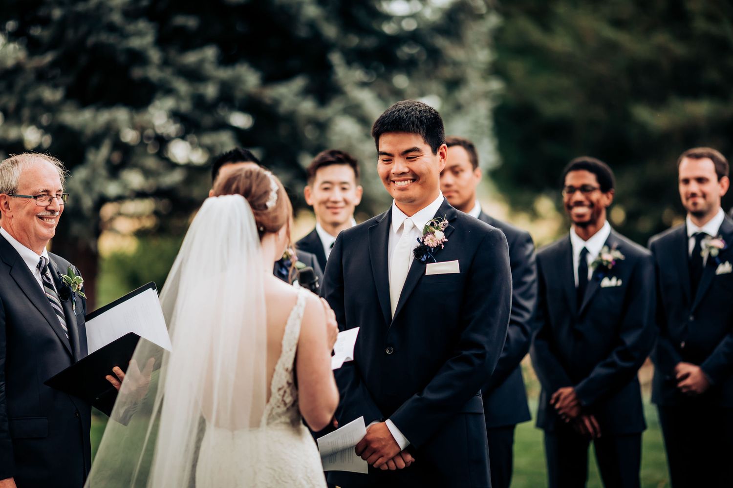 Intimate mountain wedding ceremony with couple exchanging vows under tall evergreen trees.