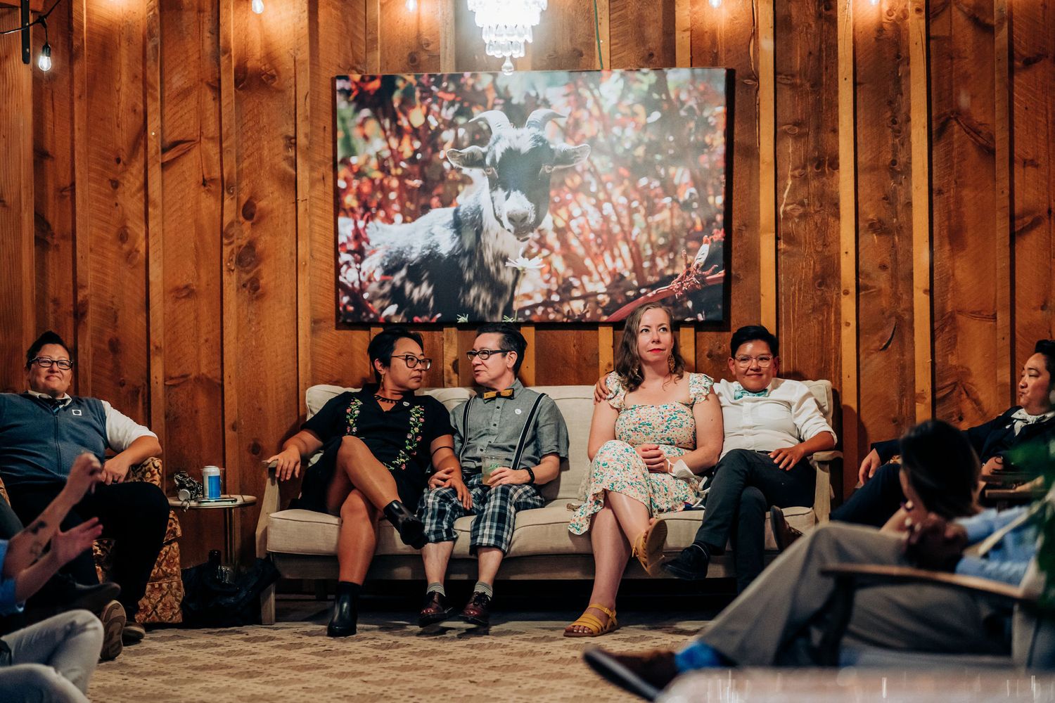 Group relaxing on couches in a cozy wood-paneled room with artwork and ambient lighting.