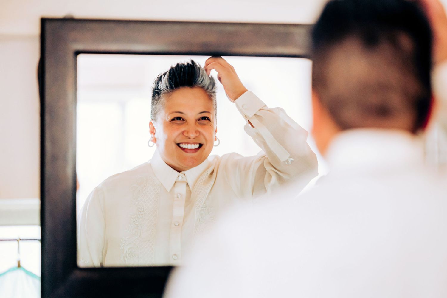 Person in white formal attire adjusting their hair in a mirror reflection.