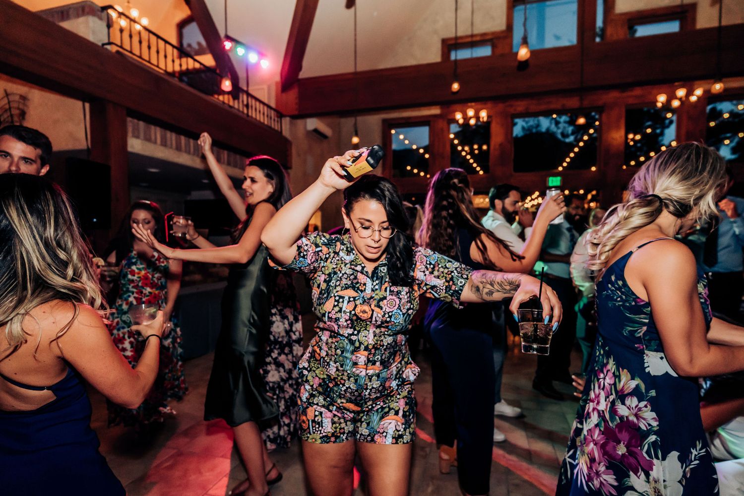 Joyful party guests dancing and celebrating on a reception dance floor with colored lighting.
