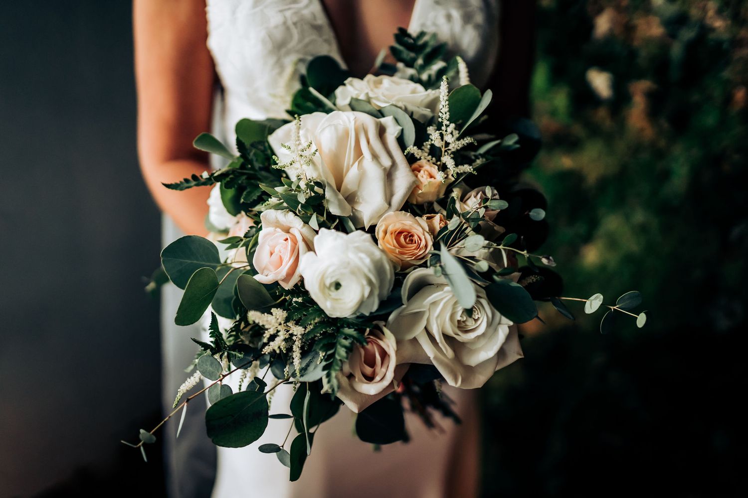 A detailed shot of an elegant bridal bouquet featuring white and blush roses with fresh eucalyptus greenery.