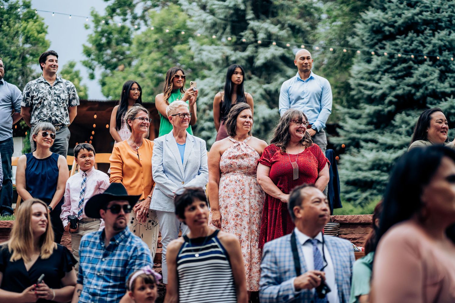 Wedding guests gather on tiered seating outdoors during a summer celebration.