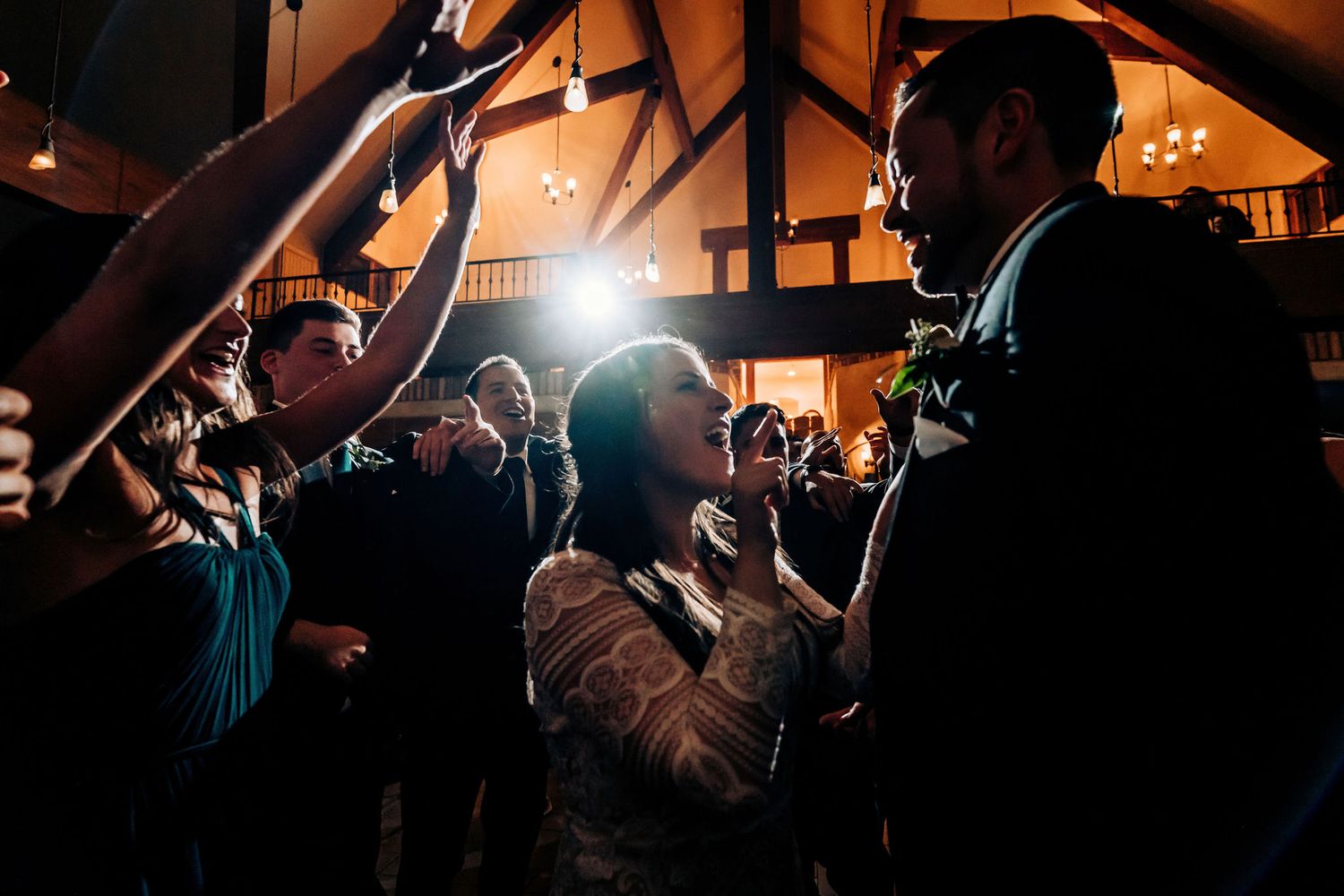 Wedding guests gather in a dark reception venue illuminated by dramatic overhead lighting.