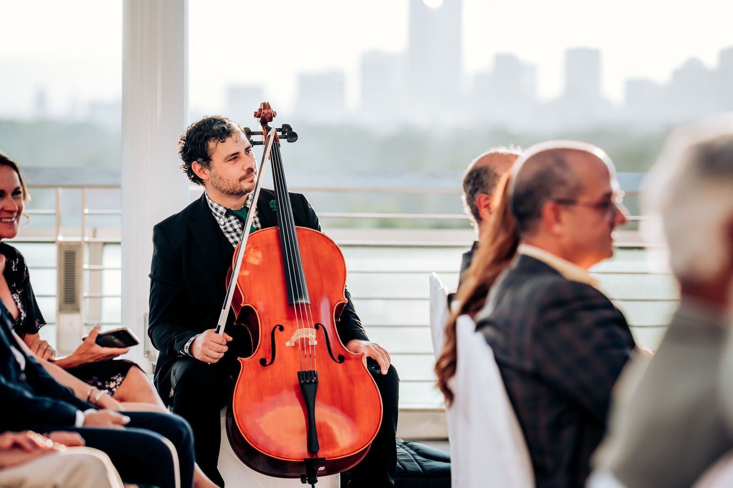 Musician playing cello during wedding ceremony with city skyline in background.