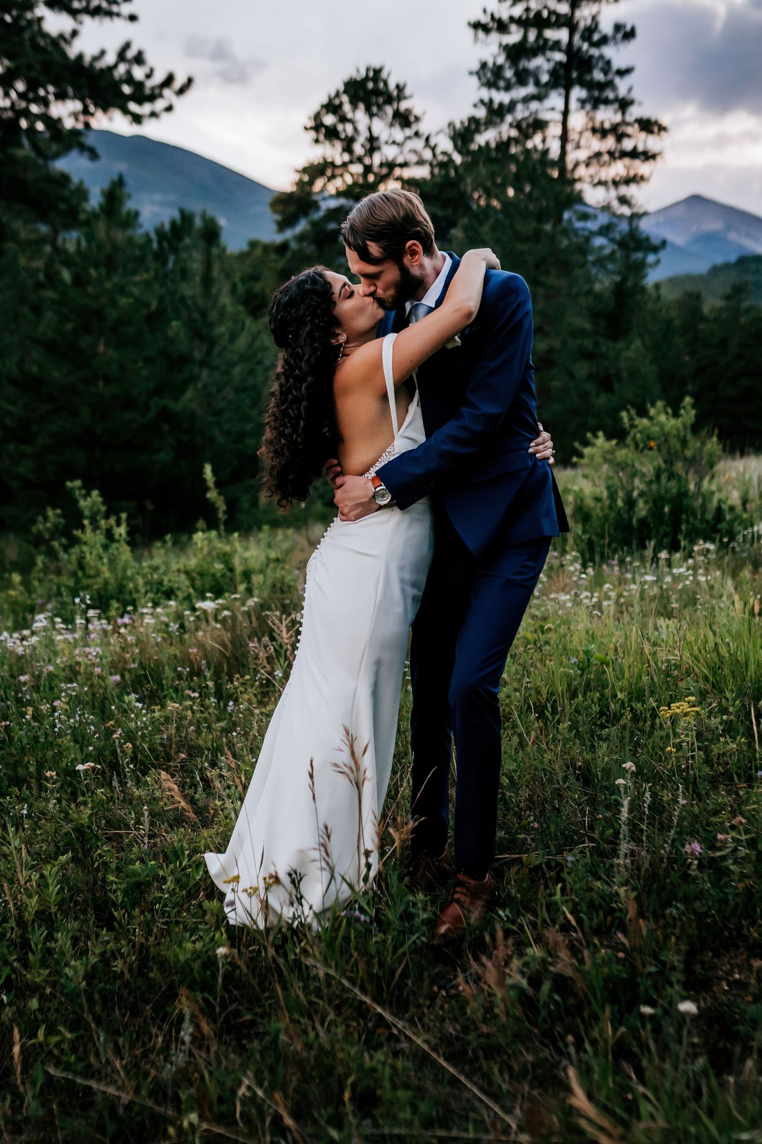 Newlyweds embrace in a wildflower meadow with mountains in the background.
