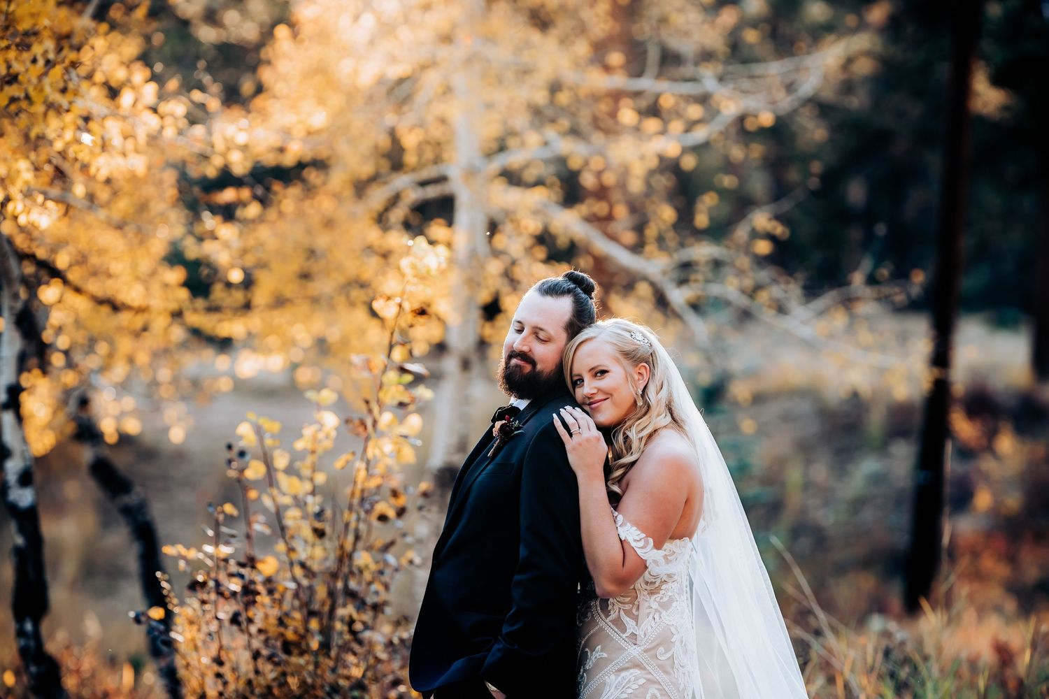 Artistic autumn wedding photo with couple embracing among golden trees.