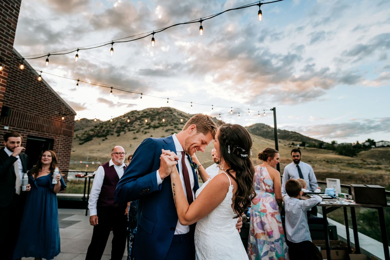 Wedding celebration under string lights at dusk with mountains in the background.