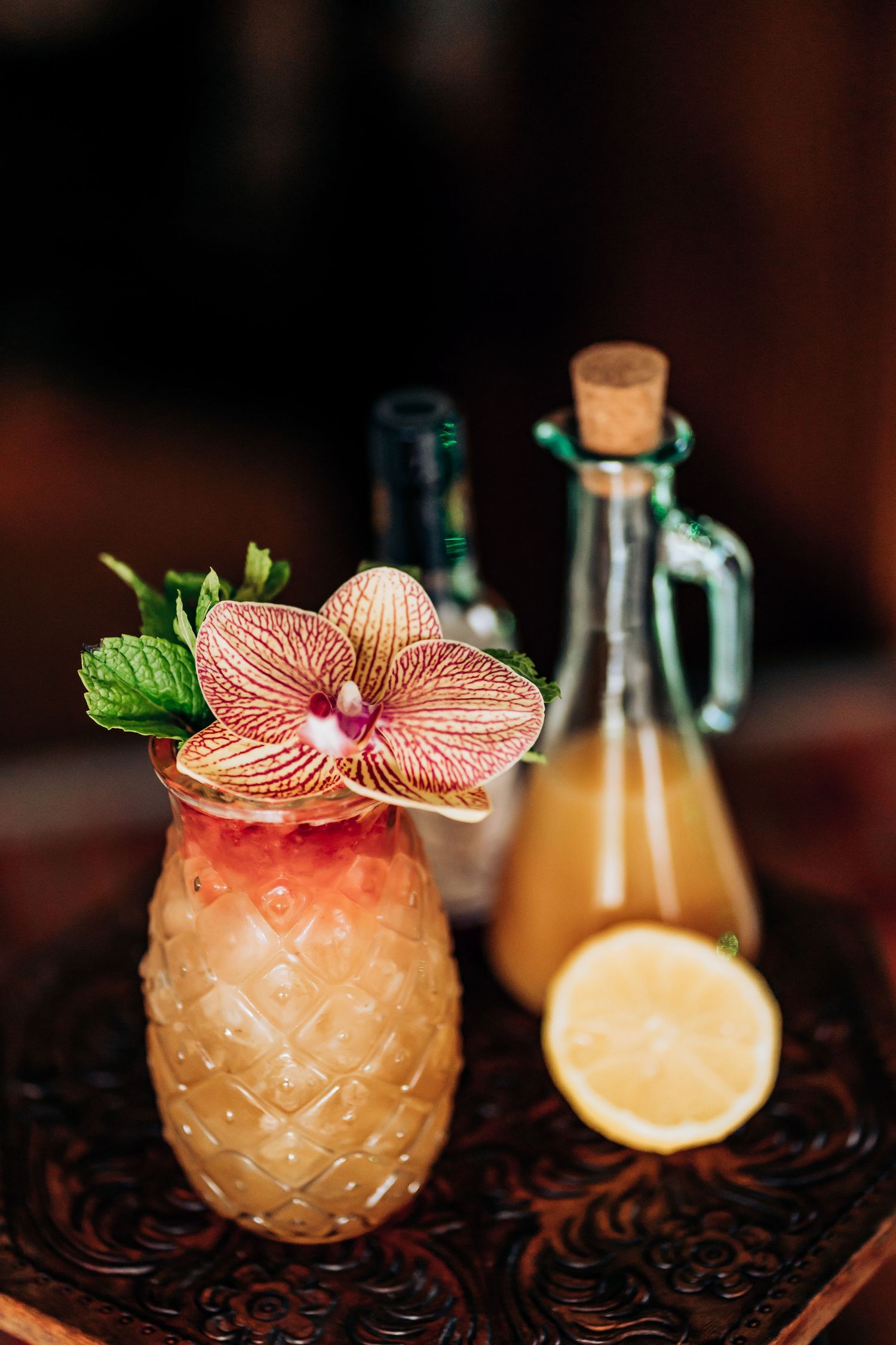 Tropical cocktail in pineapple glass garnished with orange orchid and mint leaves.