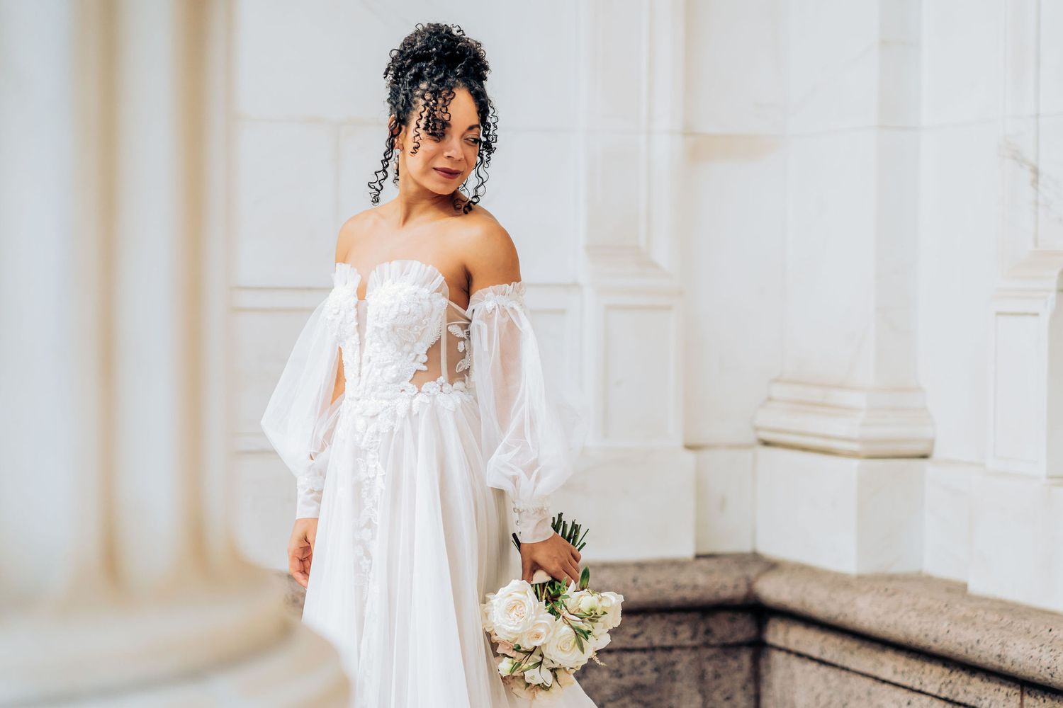 Elegant white wedding gown with delicate lace details and flowing design against light backdrop.