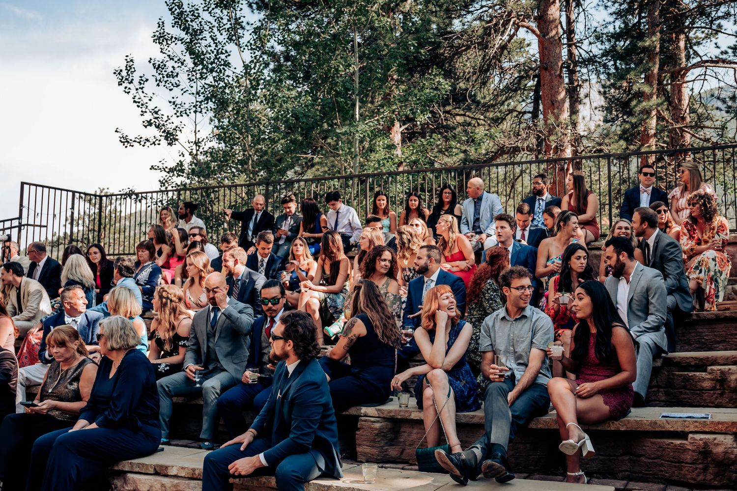 Large crowd seated on outdoor amphitheater steps surrounded by pine trees.