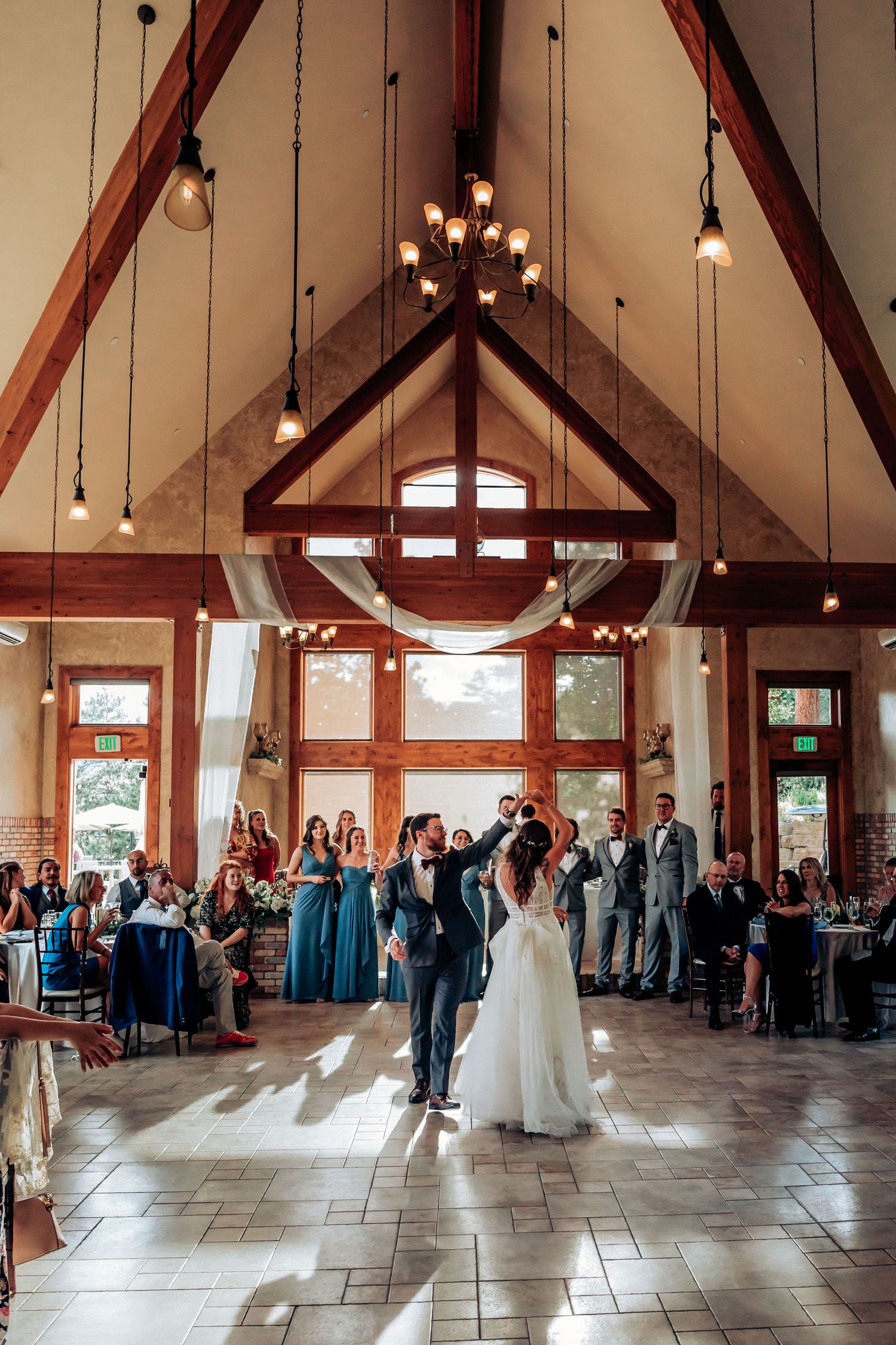 Wedding celebration in progress under vaulted ceiling with hanging lights and wooden beams.
