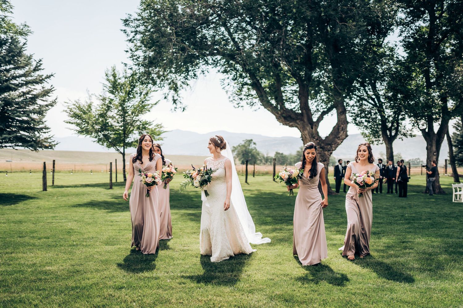 Wedding party walking and laughing together on a grassy lawn with mountain vistas.