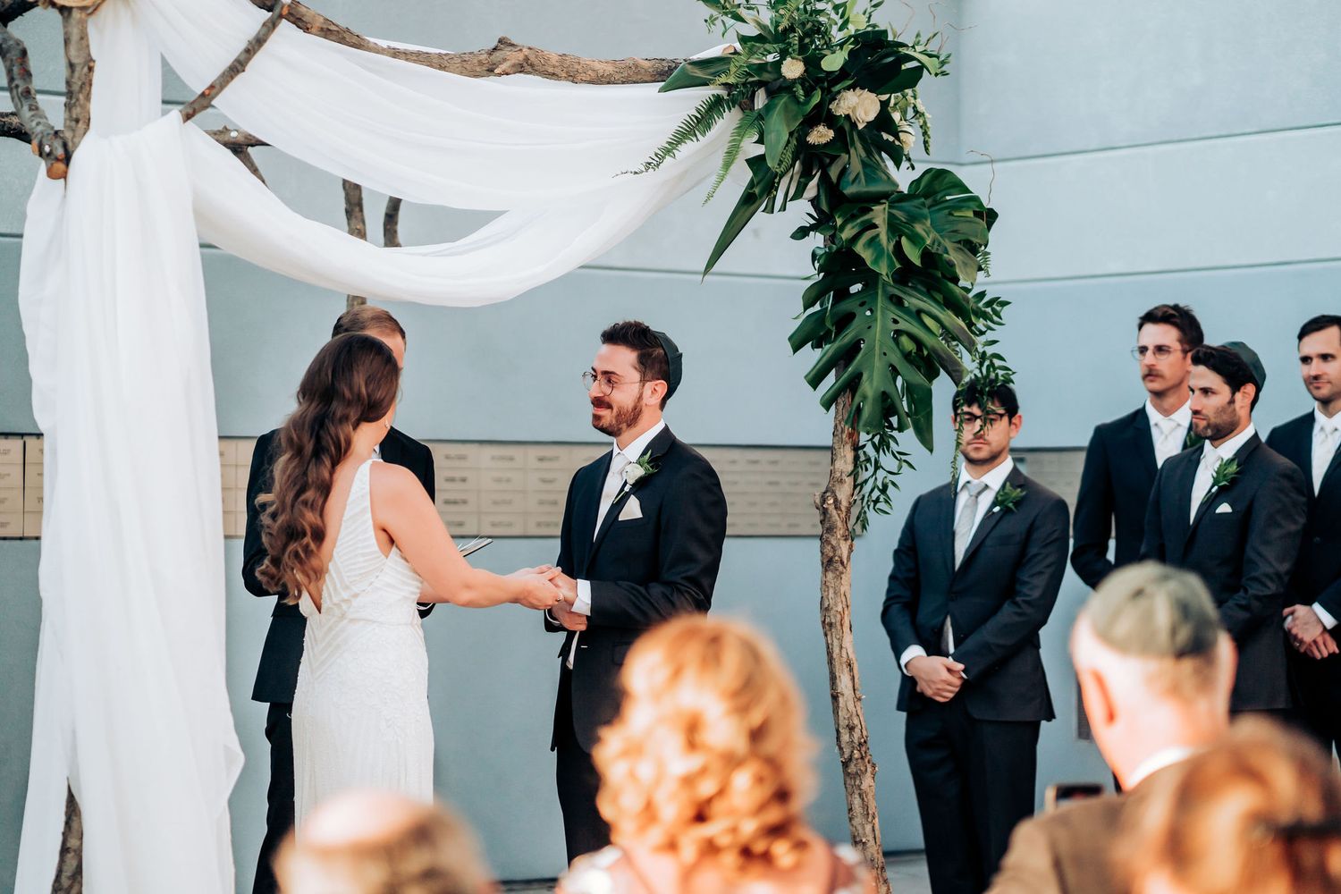 Wedding ceremony setup with white fabric arch and greenery decorations in a modern indoor space.