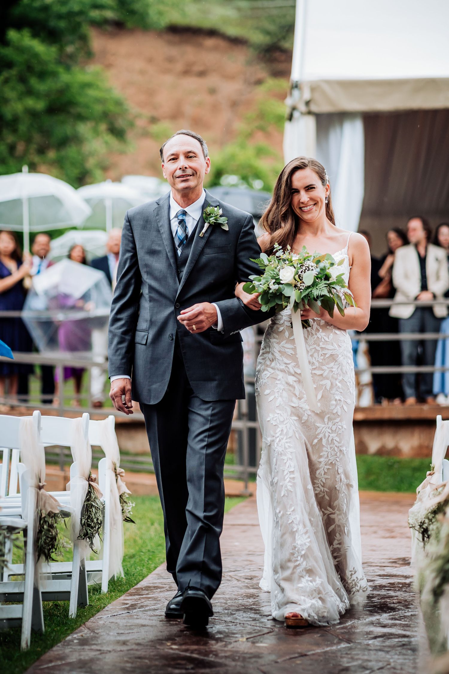 Wedding processional on a rainy day with umbrellas visible in the background.