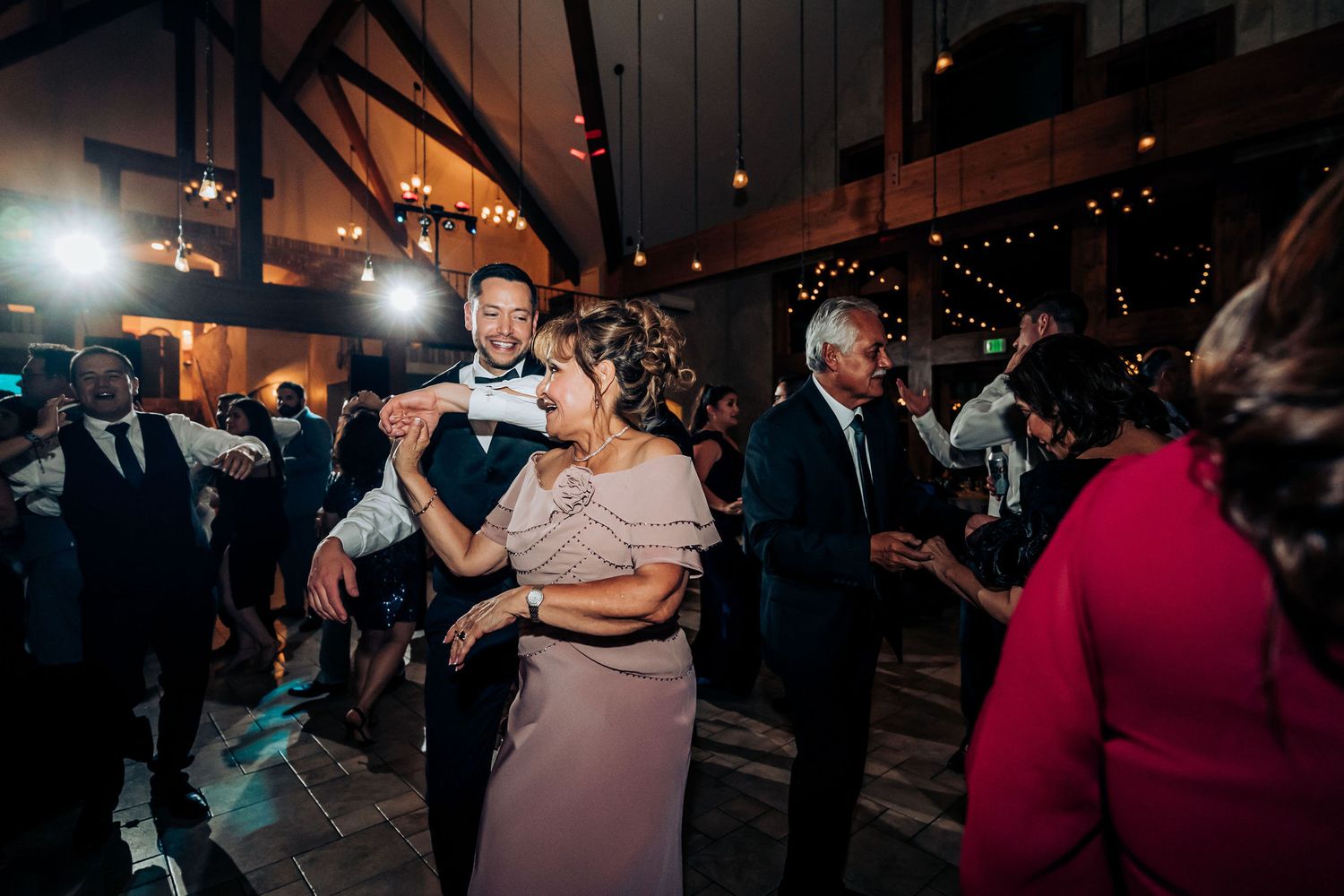 Wedding guests dancing under dramatic lighting at rustic indoor reception venue.