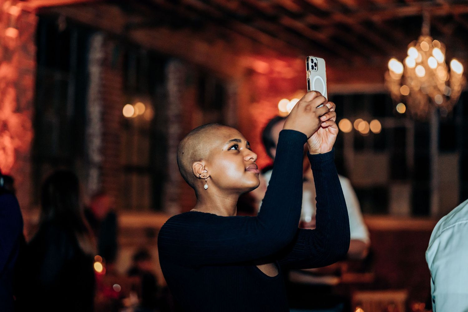 Guest capturing wedding reception moments on smartphone under warm lighting.