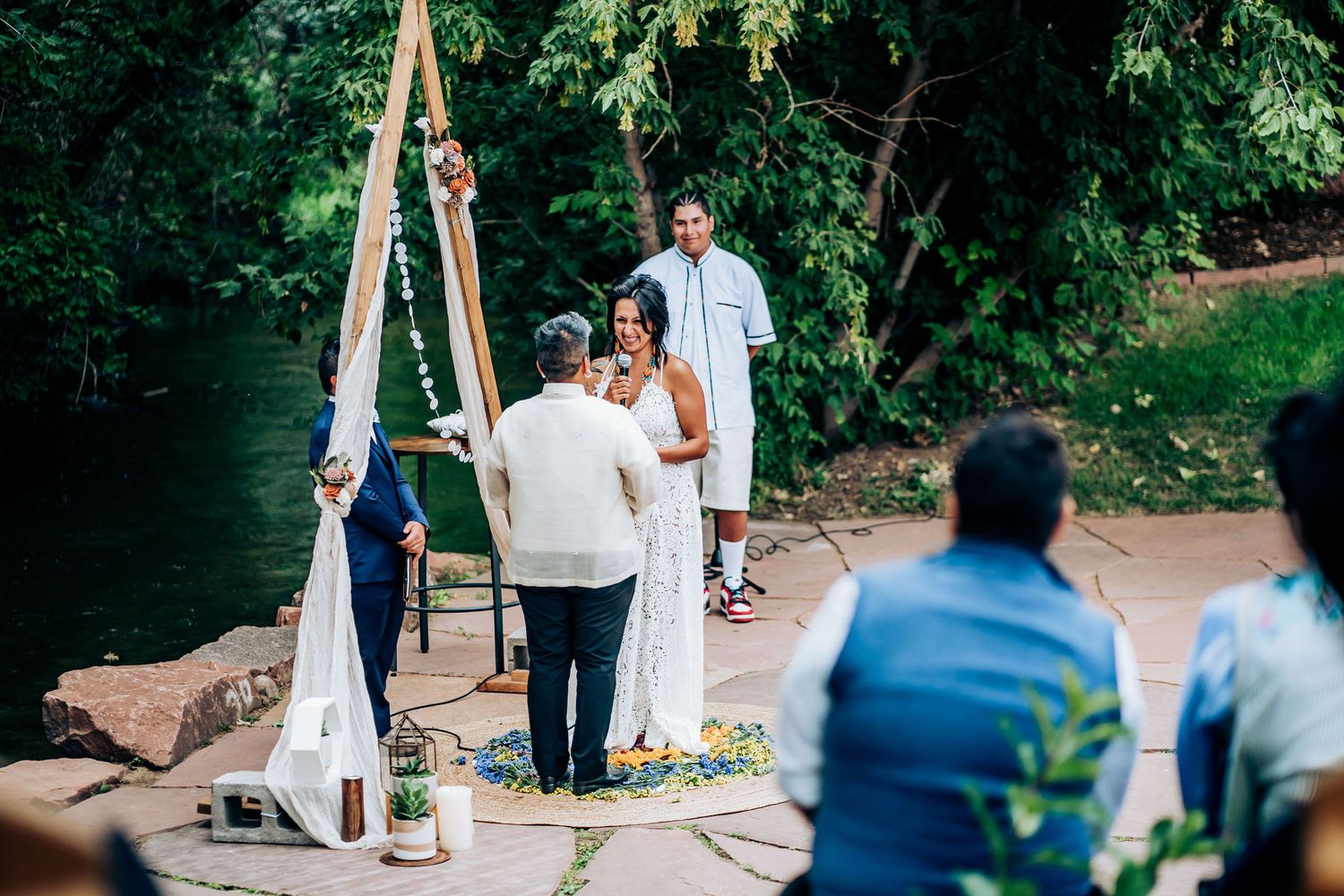 Intimate outdoor wedding ceremony with guests seated before a wooden triangle arch.