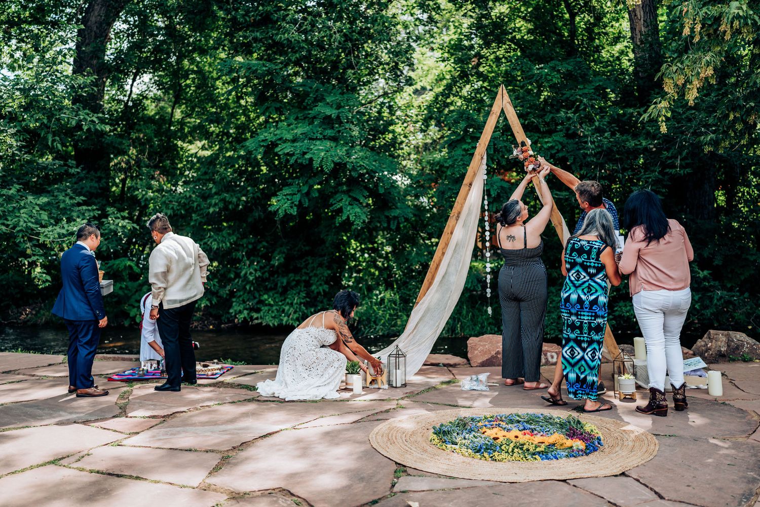 Wedding ceremony setup with a triangular arch and guests gathering on a stone patio.