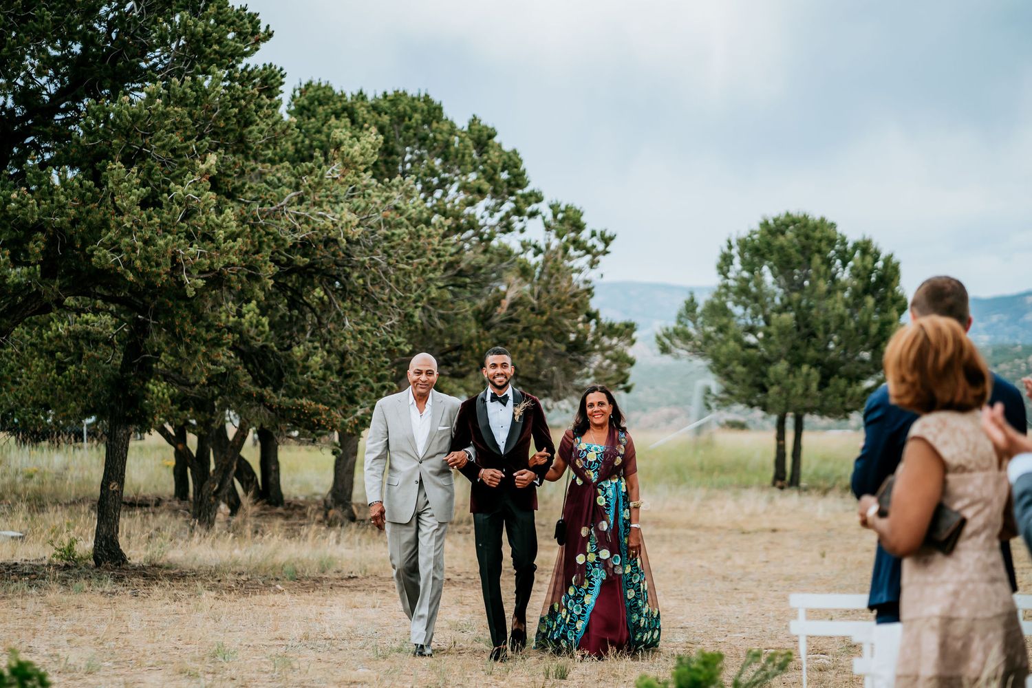 A wedding party makes their entrance during an outdoor ceremony with guests watching.