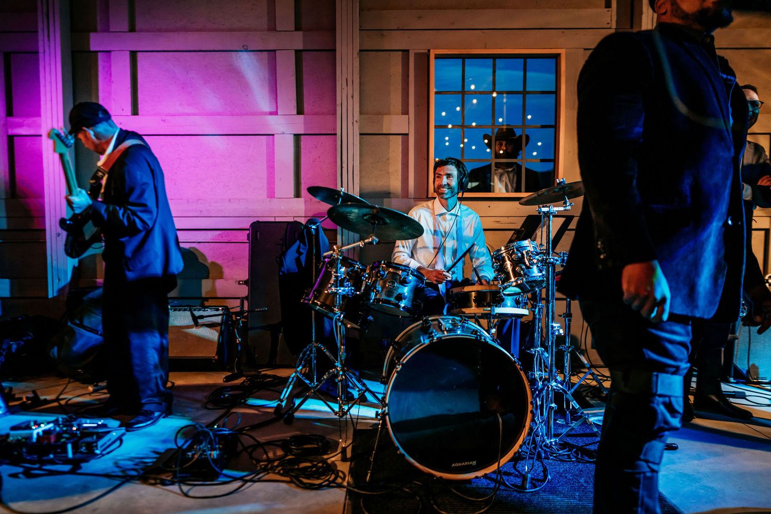 Band performing on stage with colorful lighting and drum kit.