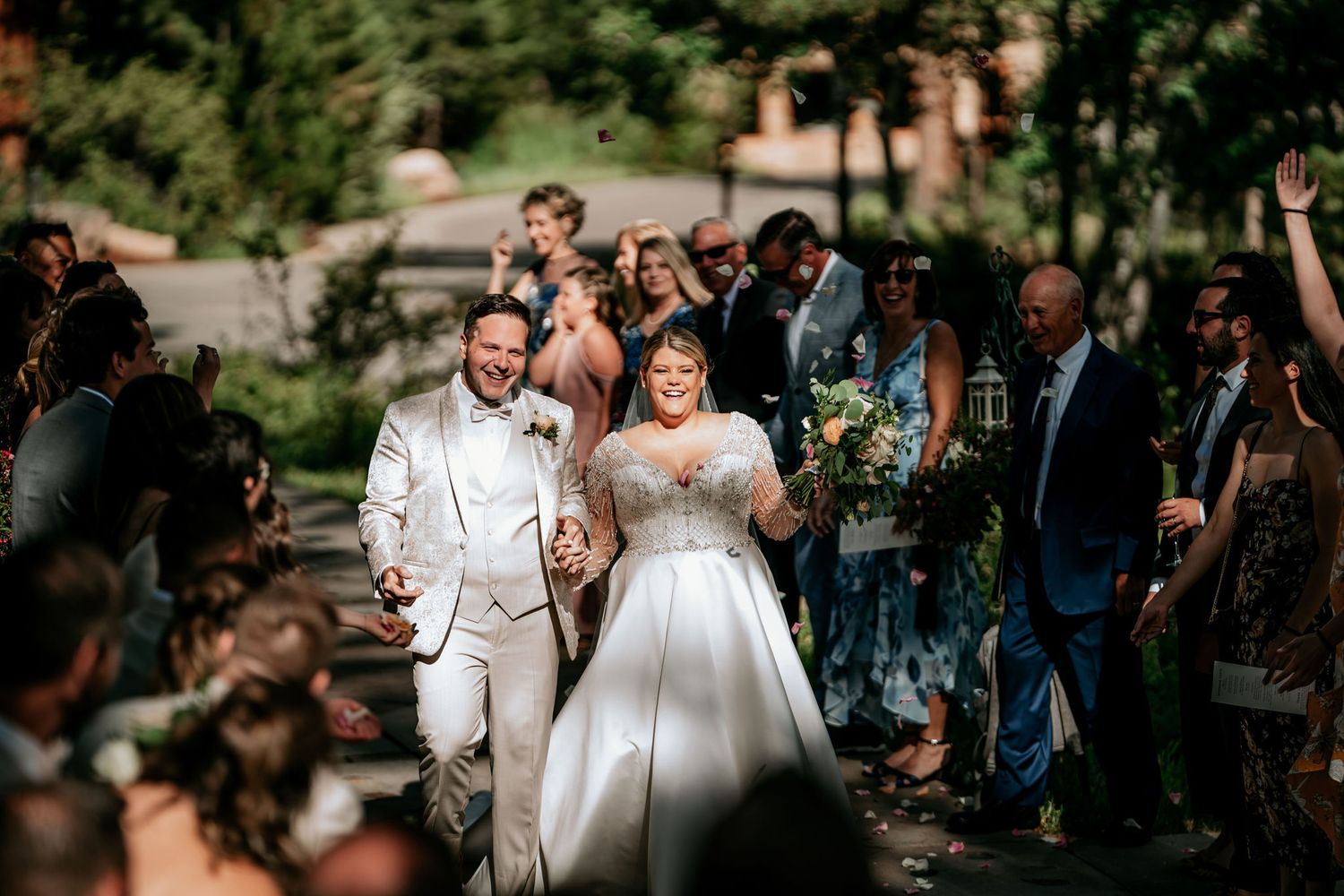 Wedding celebration with guests cheering along a sunlit outdoor path.