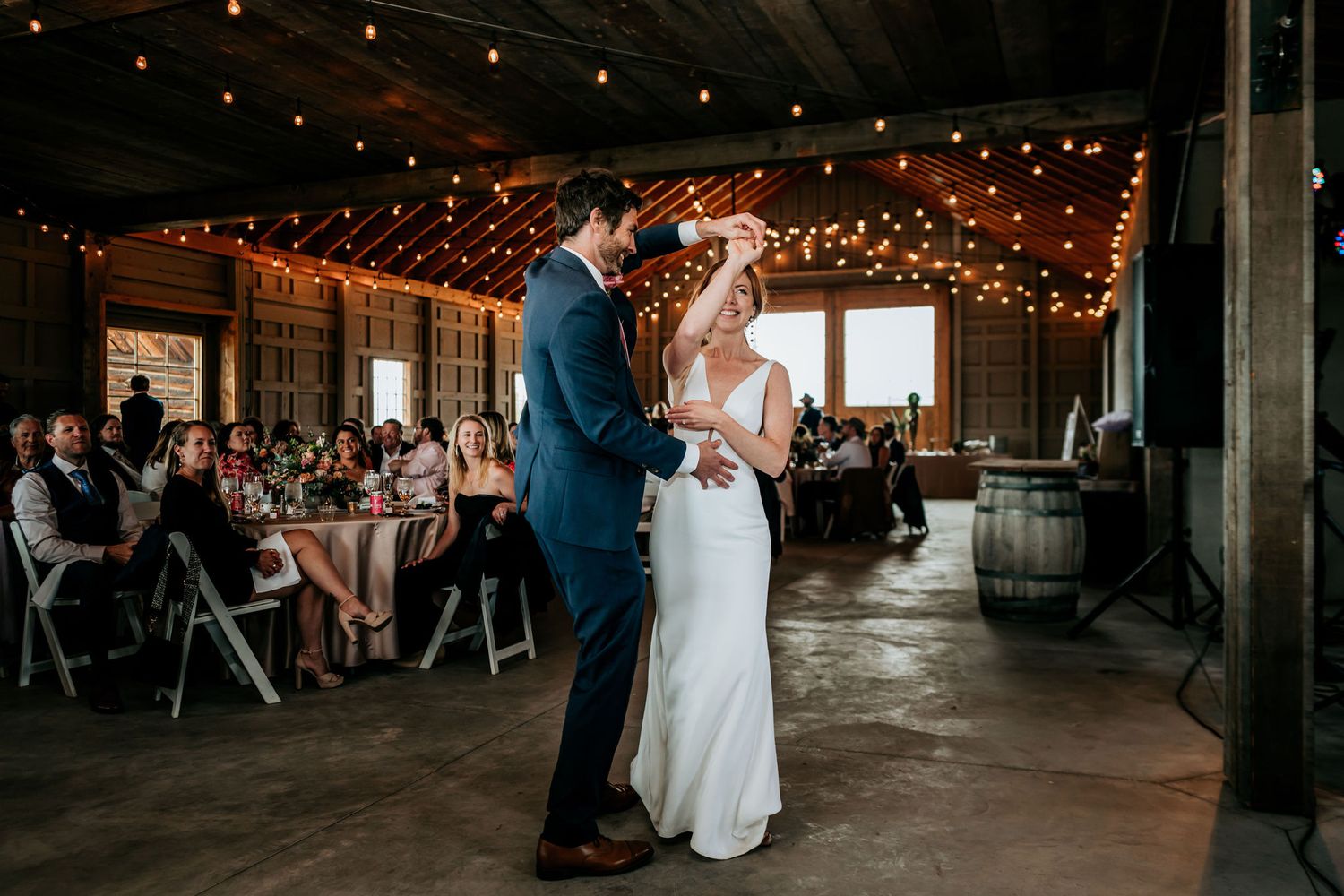 A couple dances in an intimate moment surrounded by string lights and wedding guests.