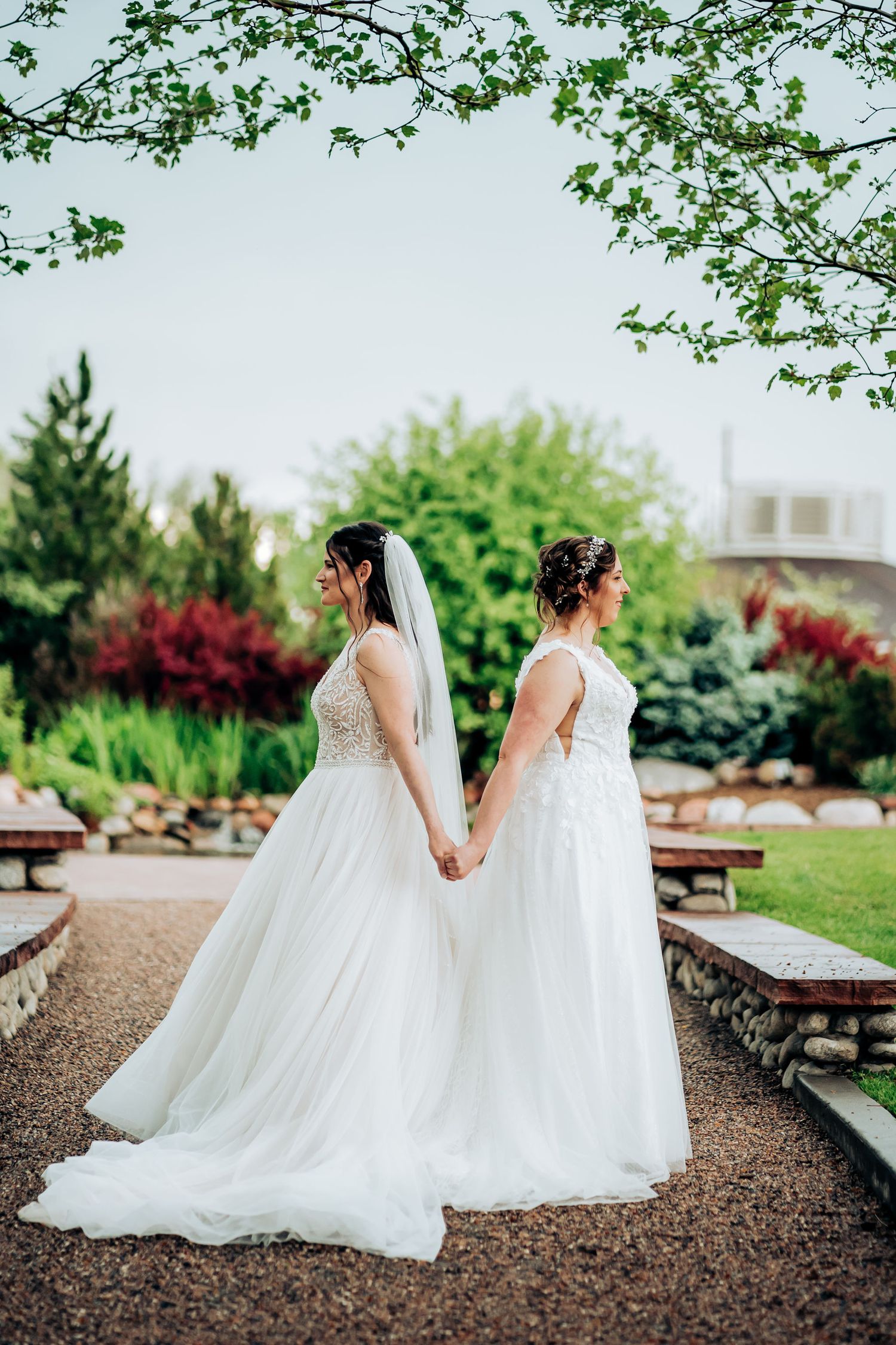 Two people in white wedding dresses holding hands in a beautiful garden setting.